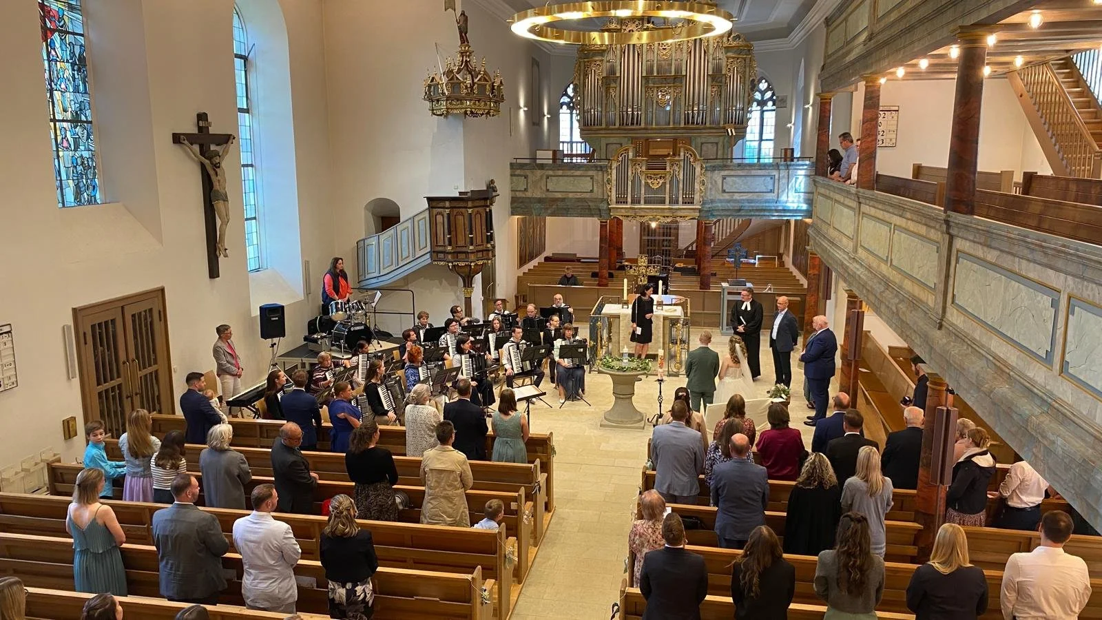 Hochzeit in einer Kirche mit einem Orchester und Brautpaar bei der Zeremonie, umgeben von Gästen.