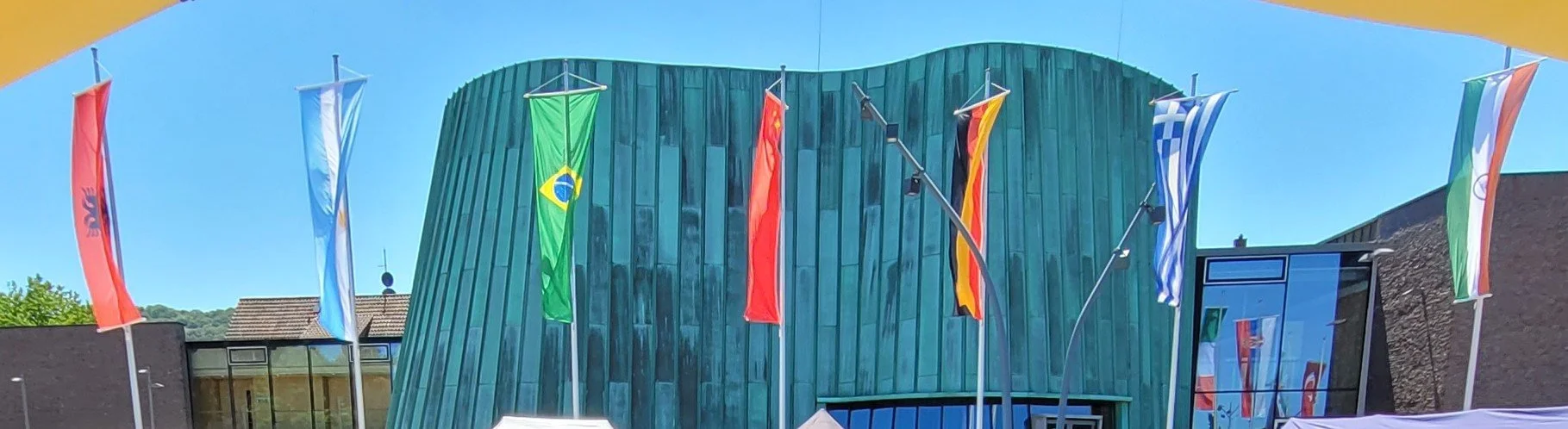 Bunte Flaggen verschiedener Länder hängen vor einem modernen Gebäude mit grüner Fassadengestaltung.