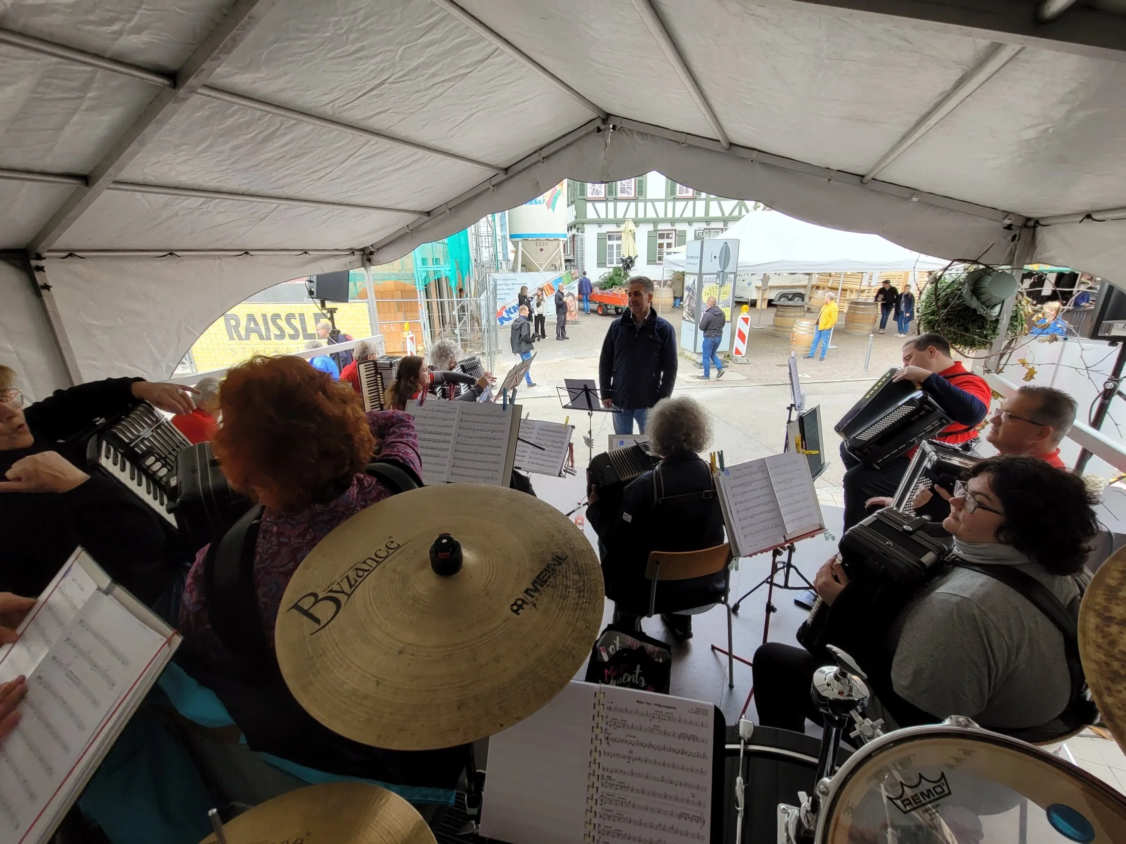 Musiker, die in einem weißen Zelt bei einem Außenmarkt spielen, mit einem Blick auf die Stadt im Hintergrund.