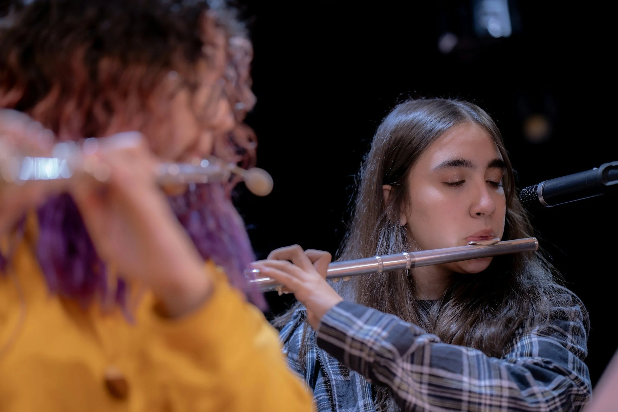 Group of women playing flutes together, focusing on a young woman with closed eyes.