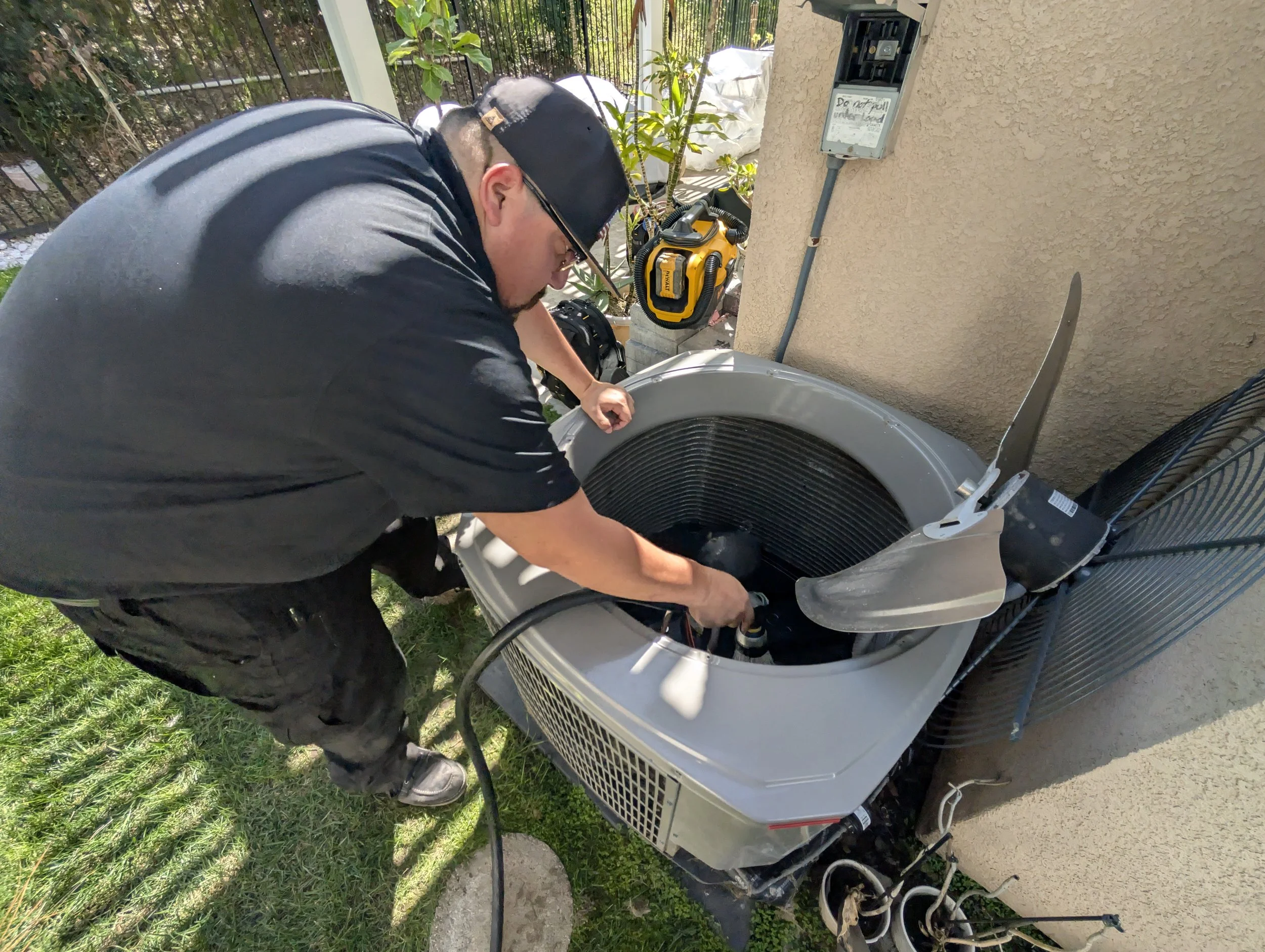A man working on an air conditioning unit outside of a house.