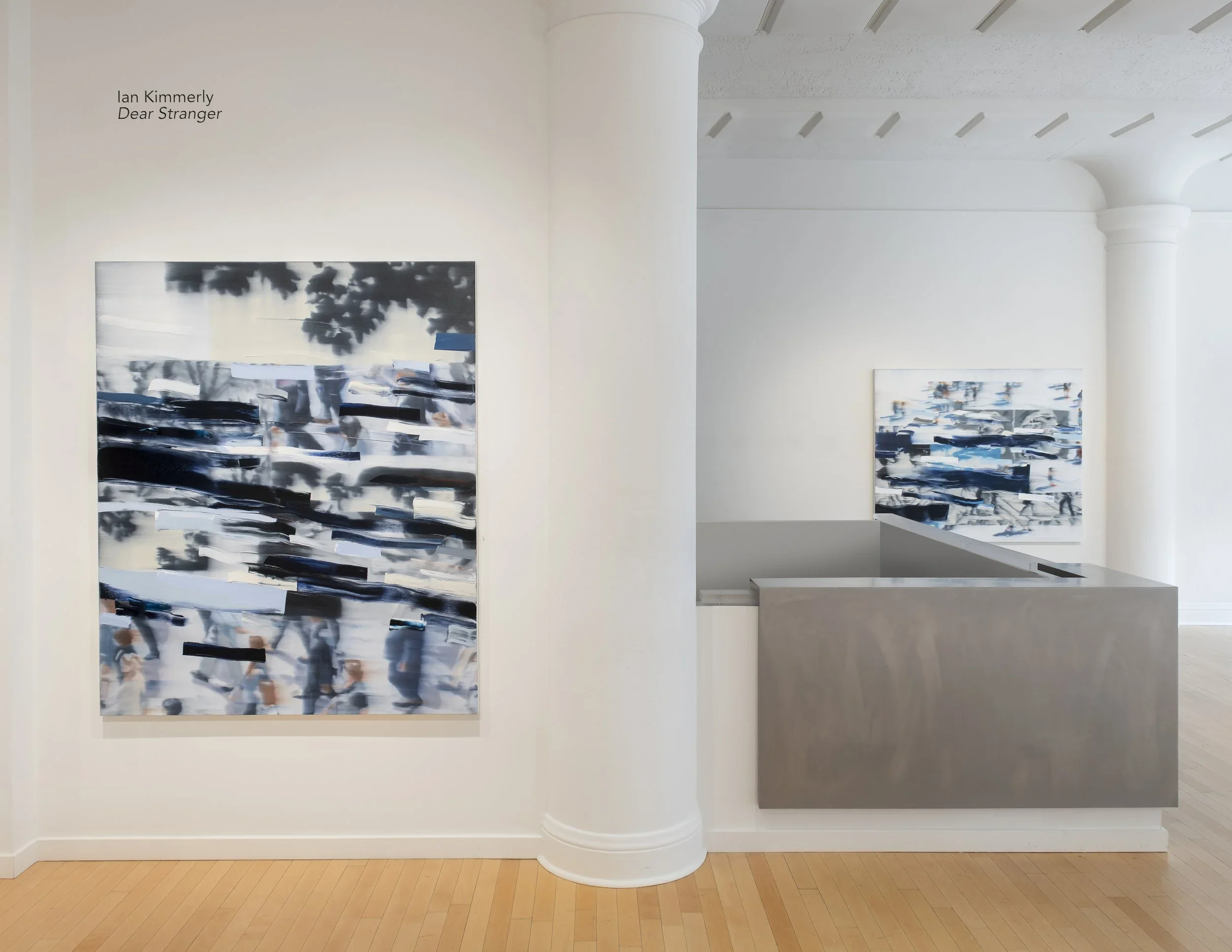 Gallery interior showing a white wall with two contemporary abstract paintings and a vintage style column. The gallery has wooden floors and a beige ceiling with wooden beams.