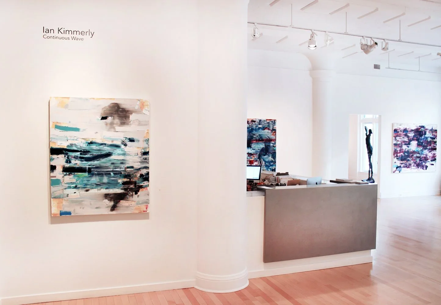 Interior view of an art gallery displaying abstract paintings and sculptures, with a reception desk and a computer.