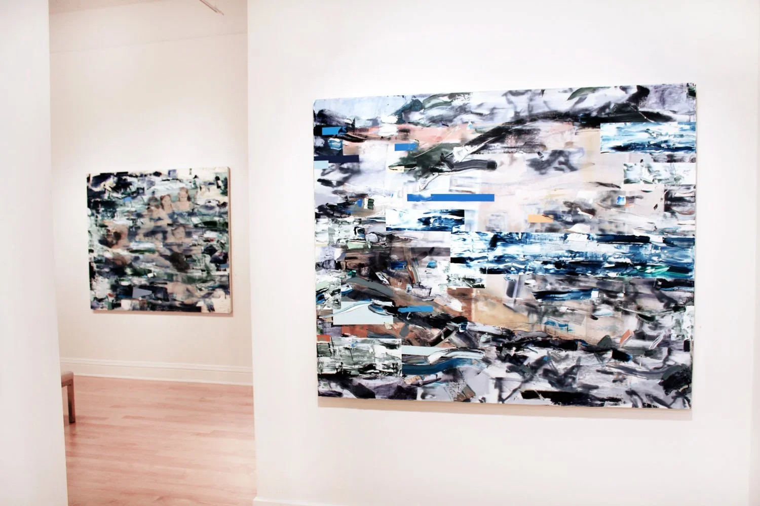 Two abstract paintings displayed on white gallery walls, featuring bold brushstrokes and a mix of colors including black, white, blue, and brown.