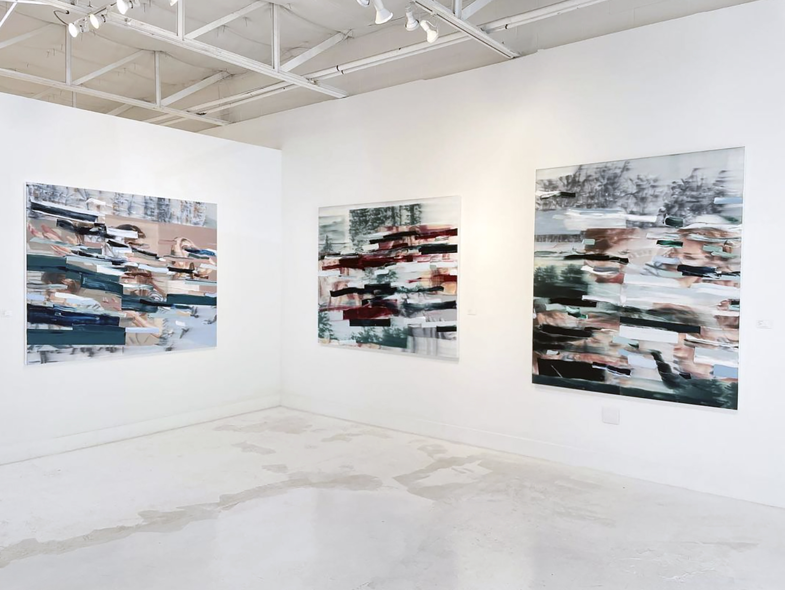 Abstract paintings displayed on a white gallery wall in an art gallery with concrete floors and white ceiling with track lighting.