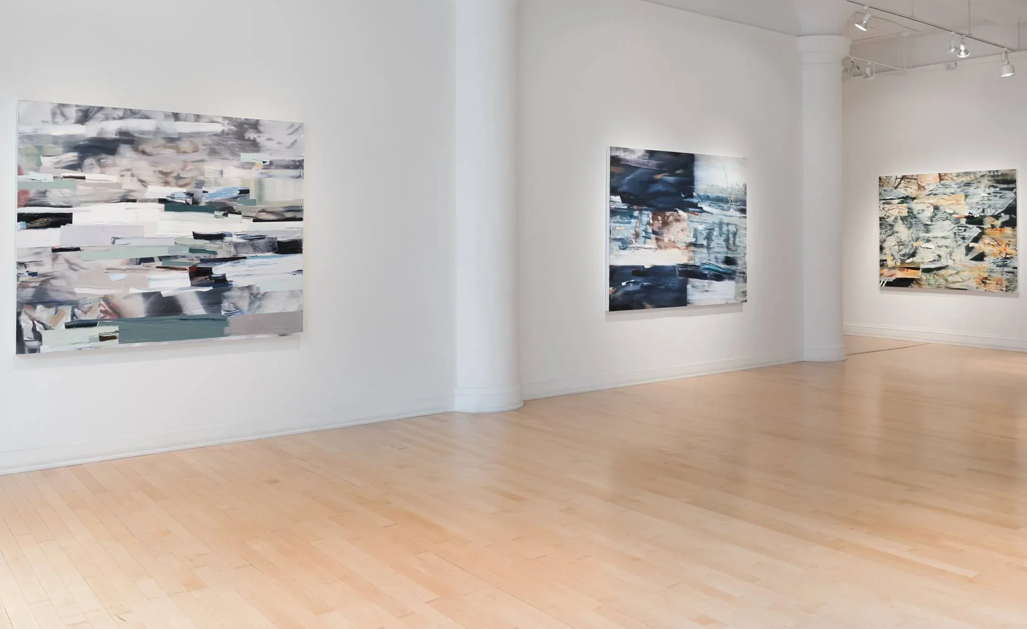 An art gallery displaying abstract paintings on white walls with hardwood floors and ceiling track lighting.