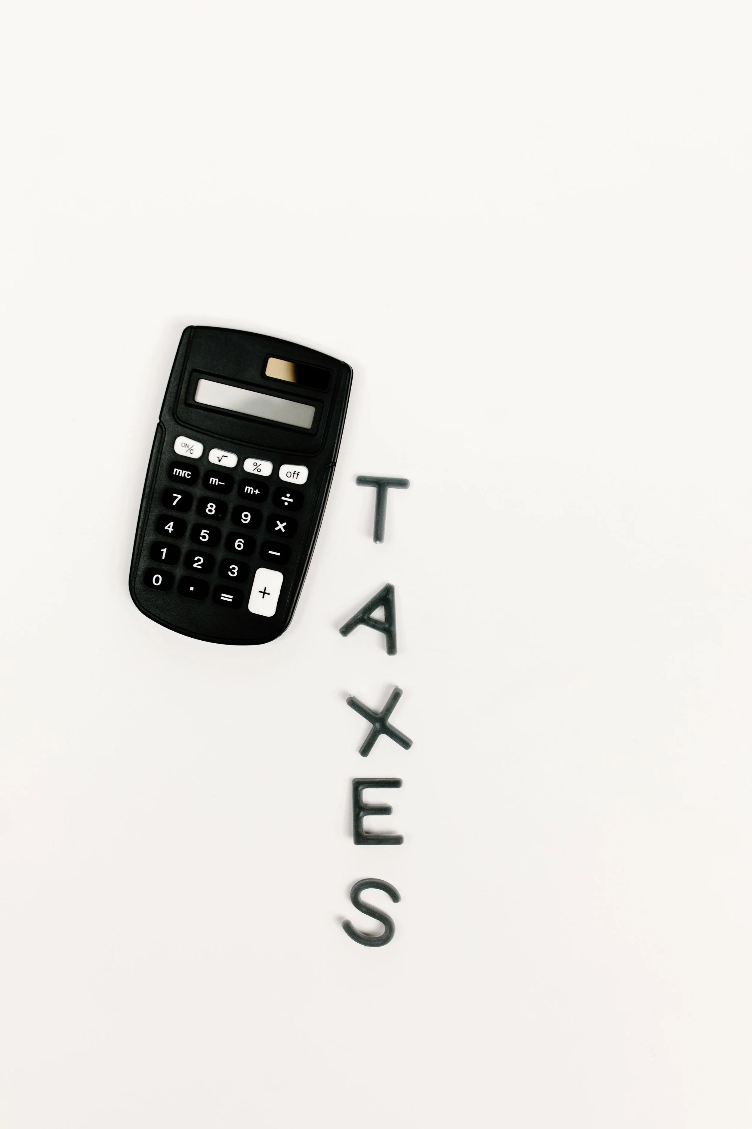 A calculator and black letter tiles spelling out the word "TAXES" on a white surface.