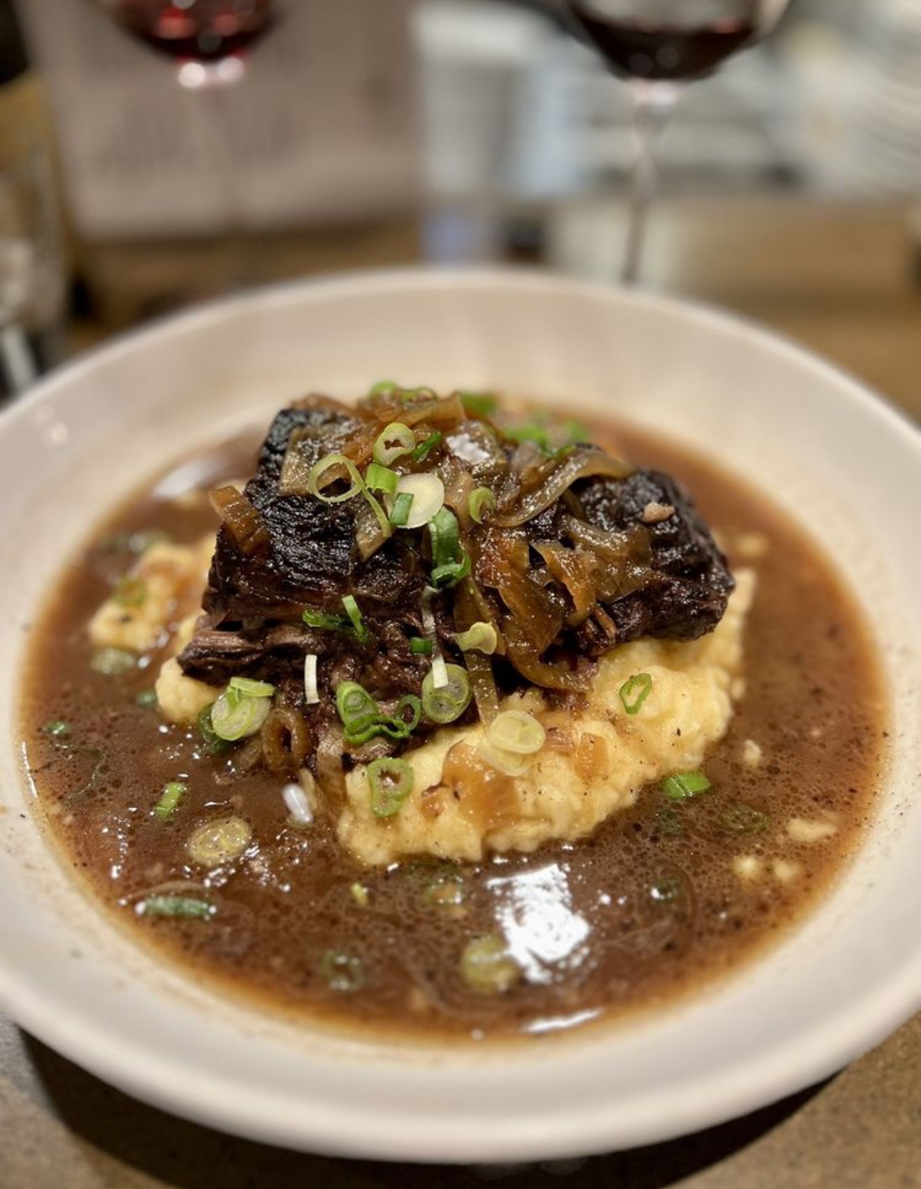A bowl of mashed potatoes topped with shredded beef, green onions, and gravy.