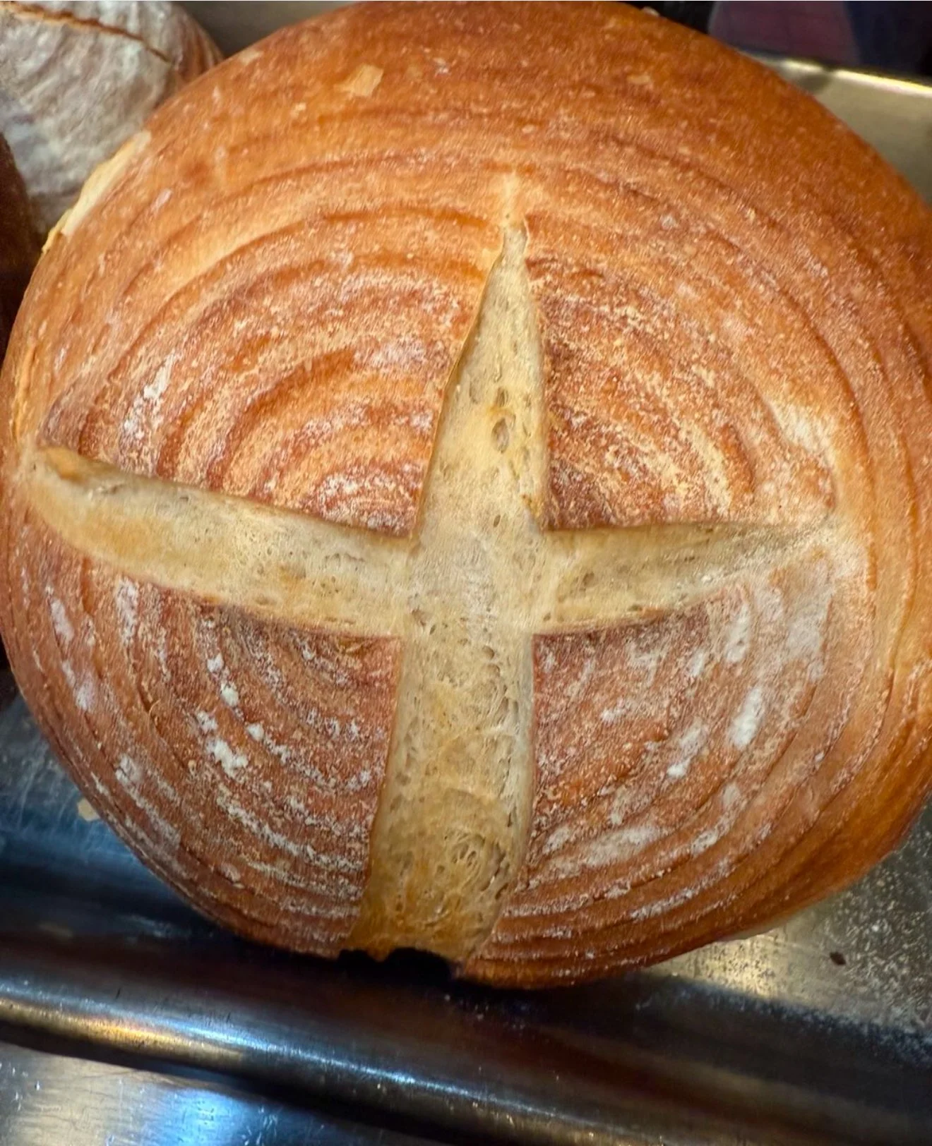 A round loaf of bread with a cross cut on the top, resting on a metal surface.