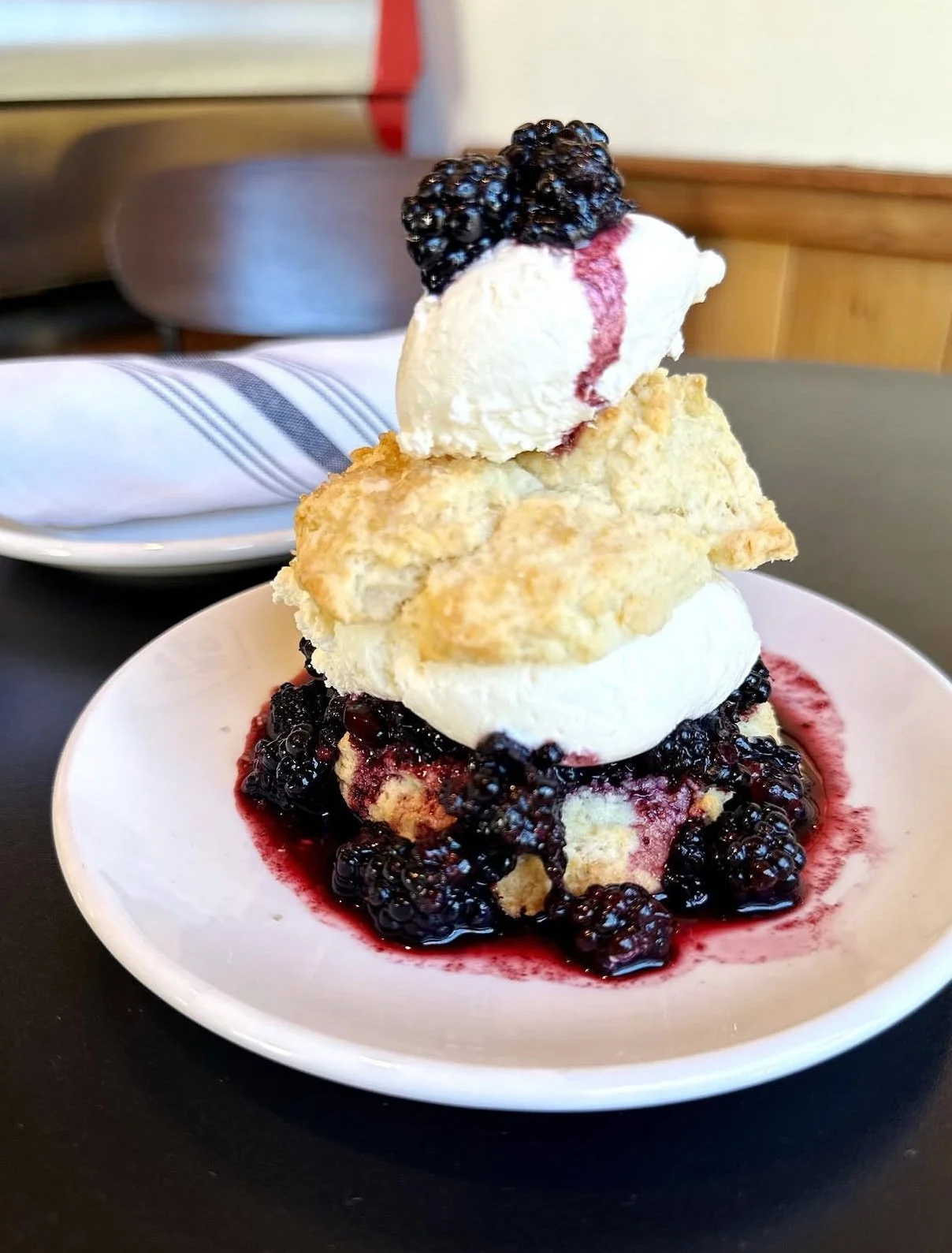 A dessert with blackberries, ice cream, and a biscuit on a white plate.