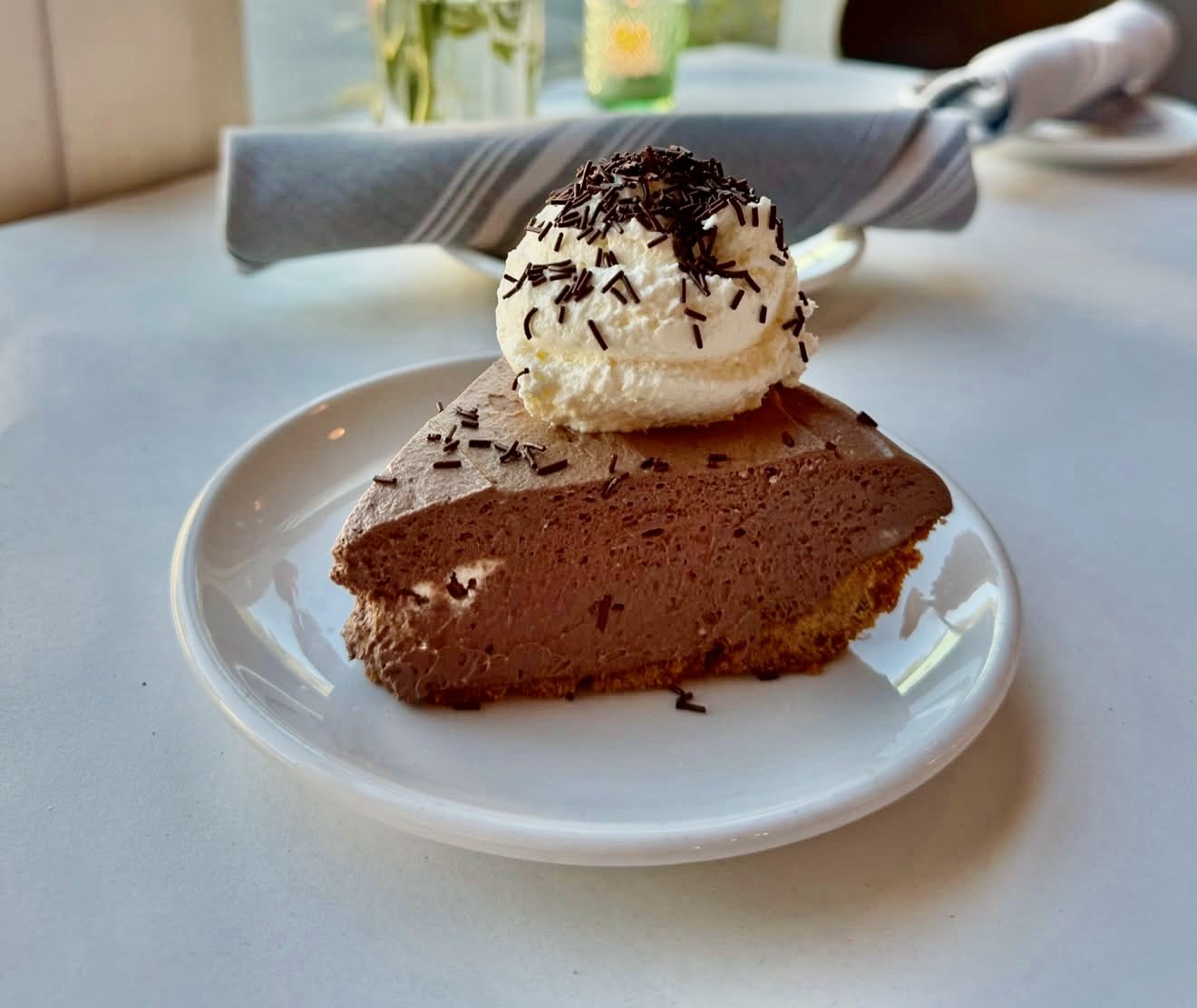 Chocolate mousse pie with a dollop of whipped cream and chocolate sprinkles on top, served on a white plate.