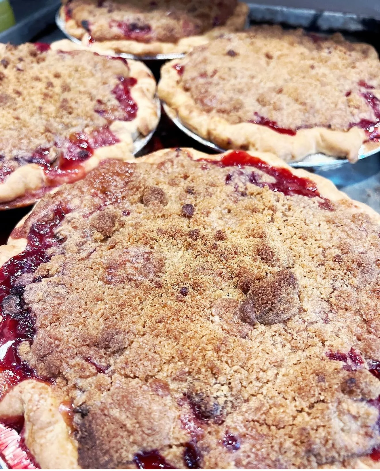 Close-up view of four cherry crumb pies with golden brown crumb topping and cherry filling.