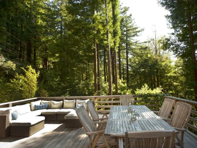 Outdoor wooden deck in Monte Rio with a dining table and chairs, surrounded by a forest with tall green trees
