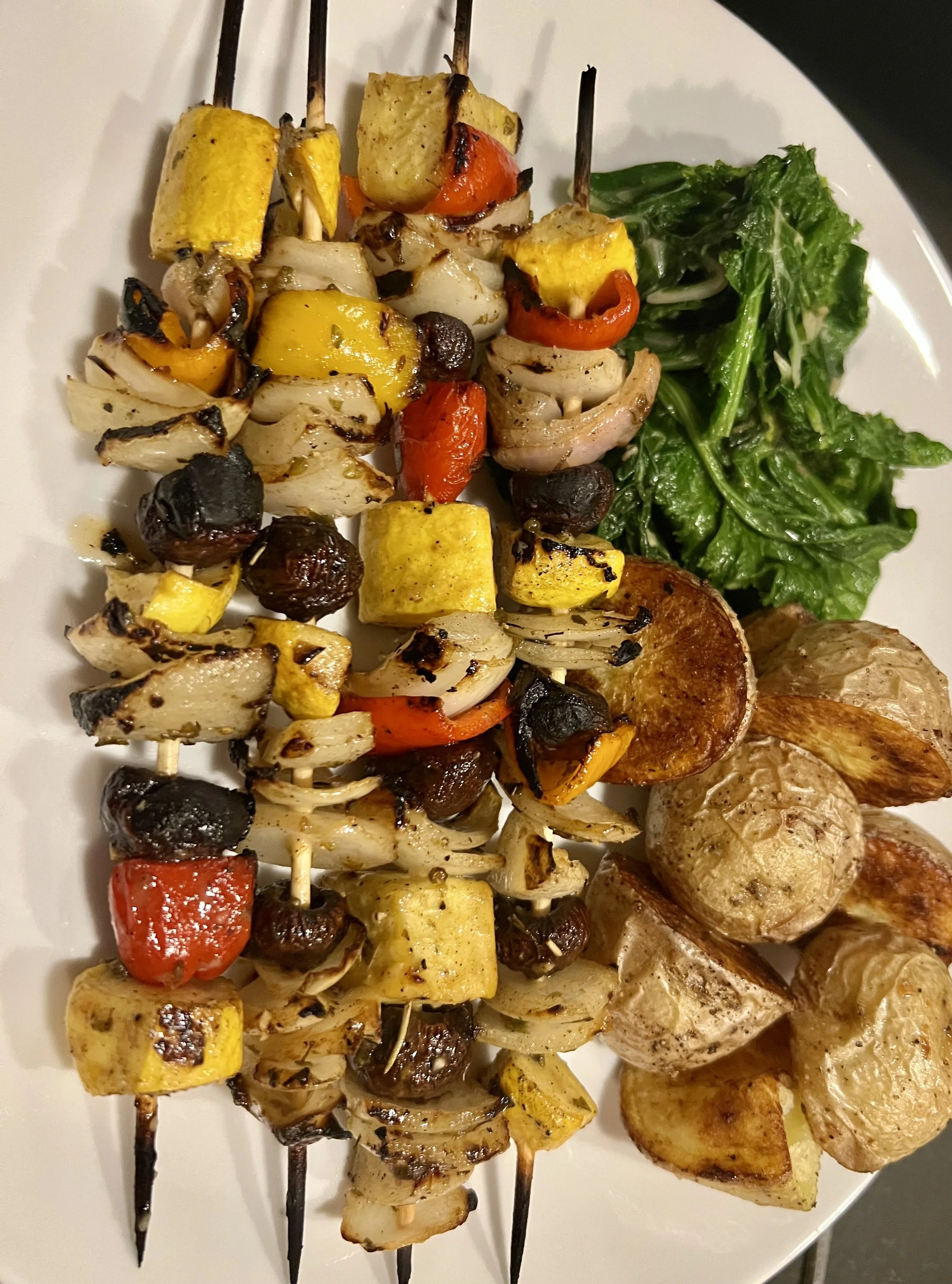 Food from Chef David Karlin featuring skewers with grilled vegetables, including yellow squash, cherry tomatoes, cherry peppers, onions, and black olives, placed next to a side of leafy green salad on a white plate.