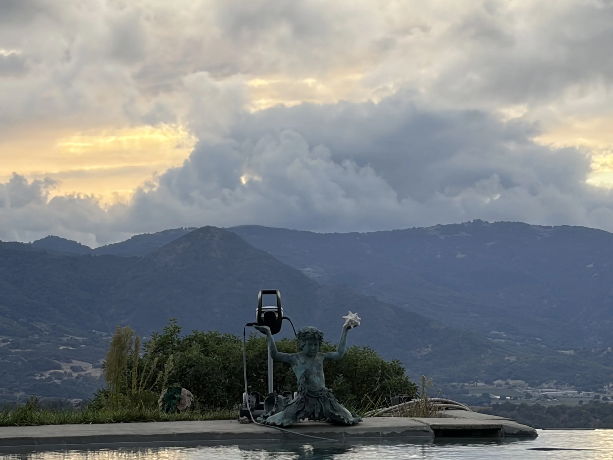 Statue oholding a star and a torch, with a scenic mountainous landscape and cloudy sky in the background.