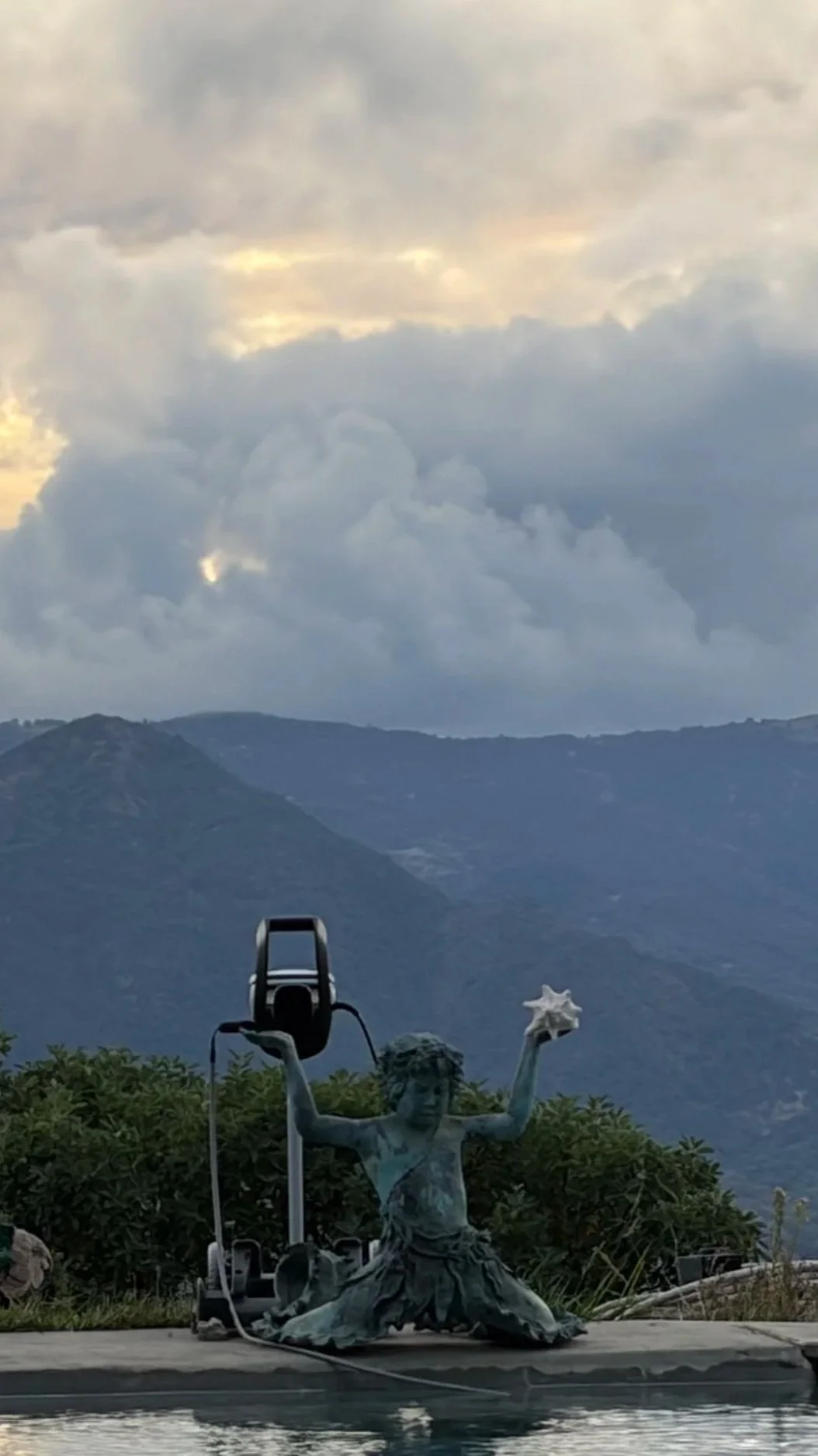 A scenic mountain view in the northern corner of Sonoma County with large clouds in the sky, a statue of a mermaid holding a trident, and a tanning bed in the foreground.