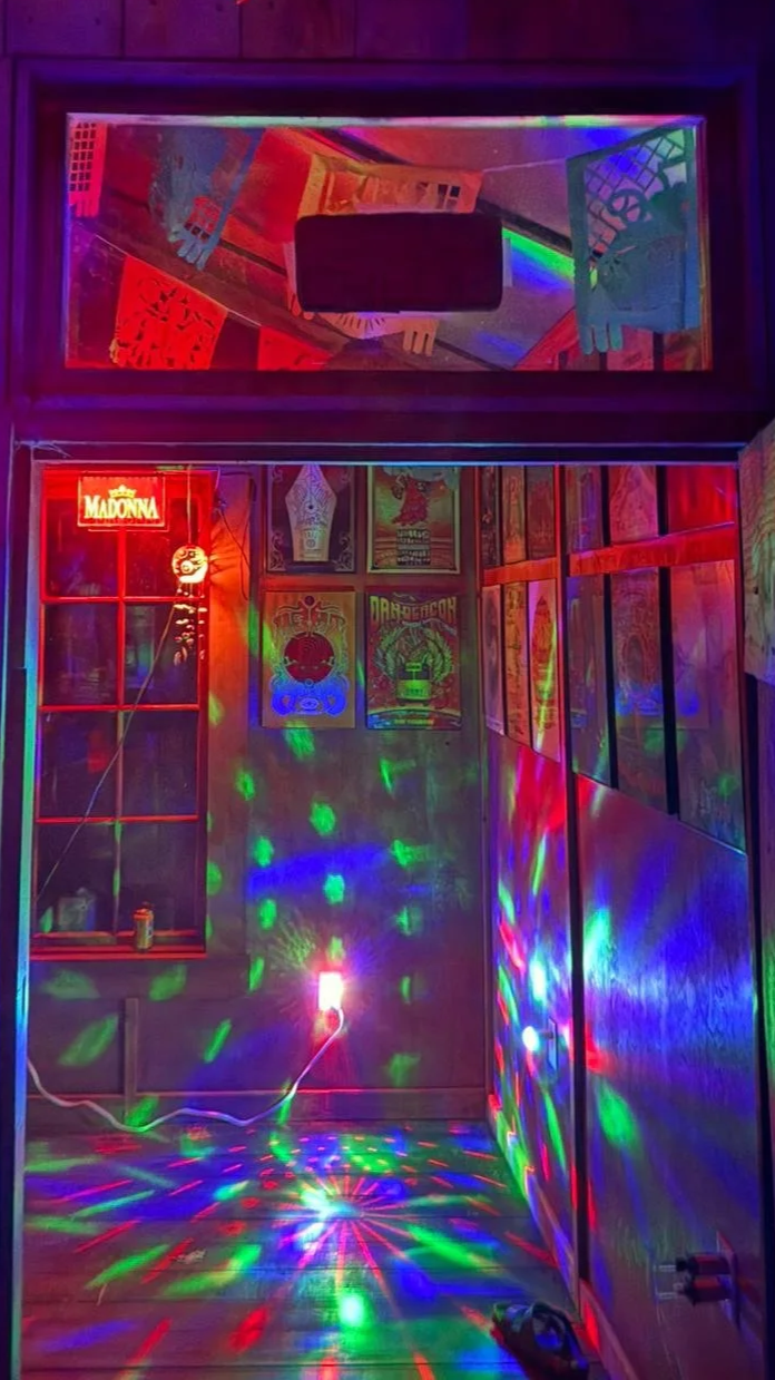 Colorful disco lights illuminating a small secret bar with posters on the wall and a Madonna neon sign.