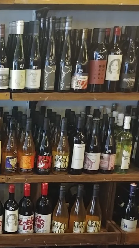 Shelf filled with various bottles of wine organized by type and label, with dark and light-colored wines visible.