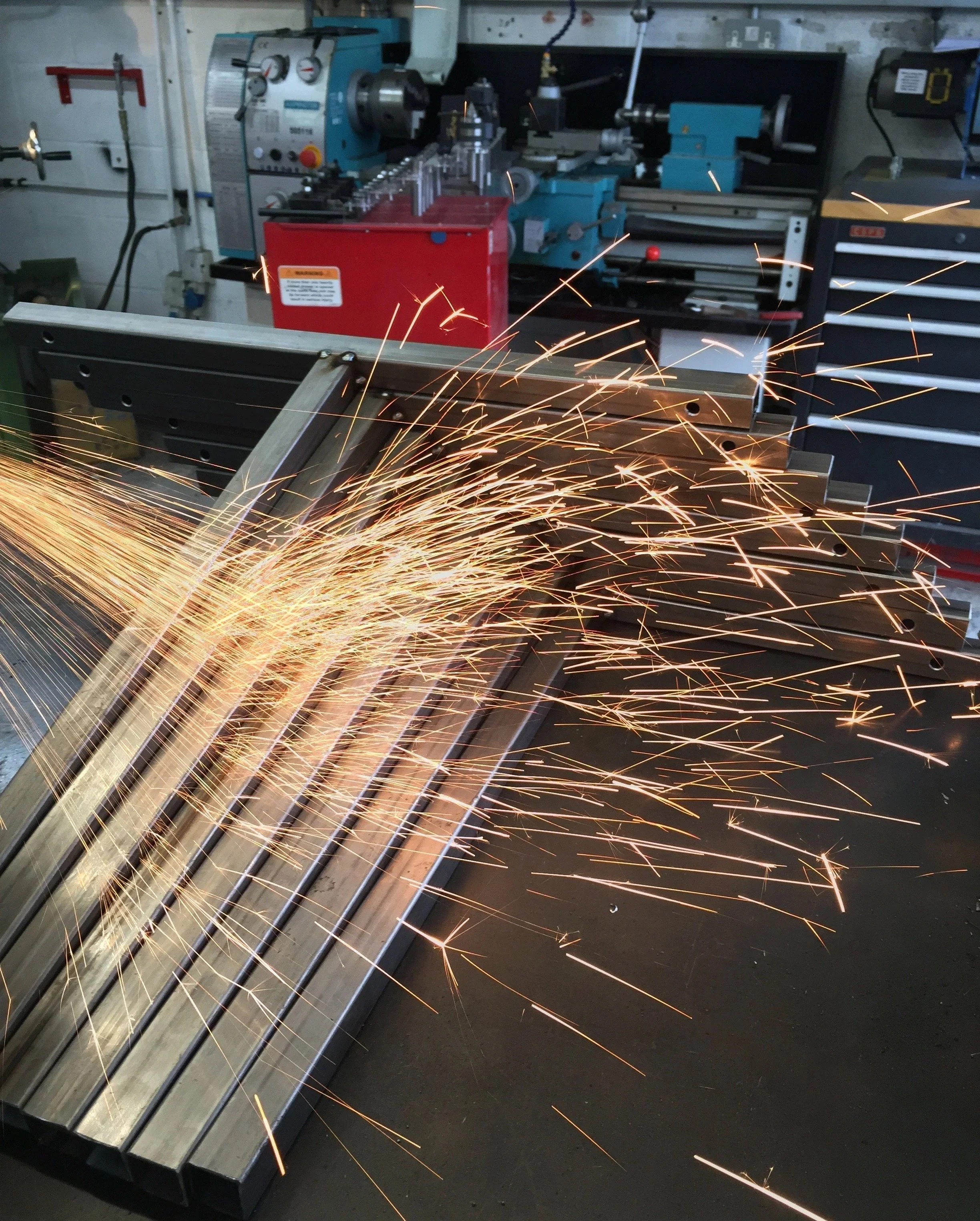 A workshop with a metalwork lathe, metal rods, and sparks from metal grinding or welding.