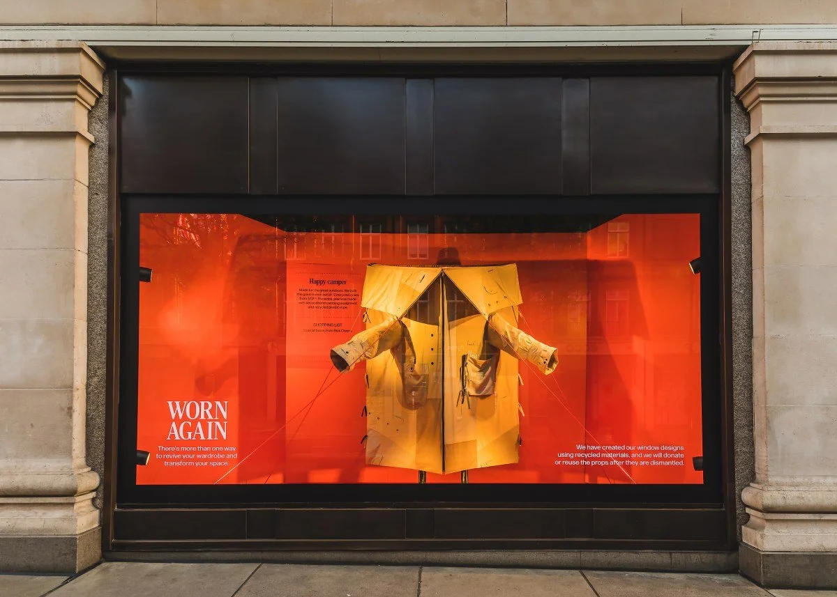 Display window showcasing a yellow camping tent with orange background, promoting sustainable outdoor gear reuse.