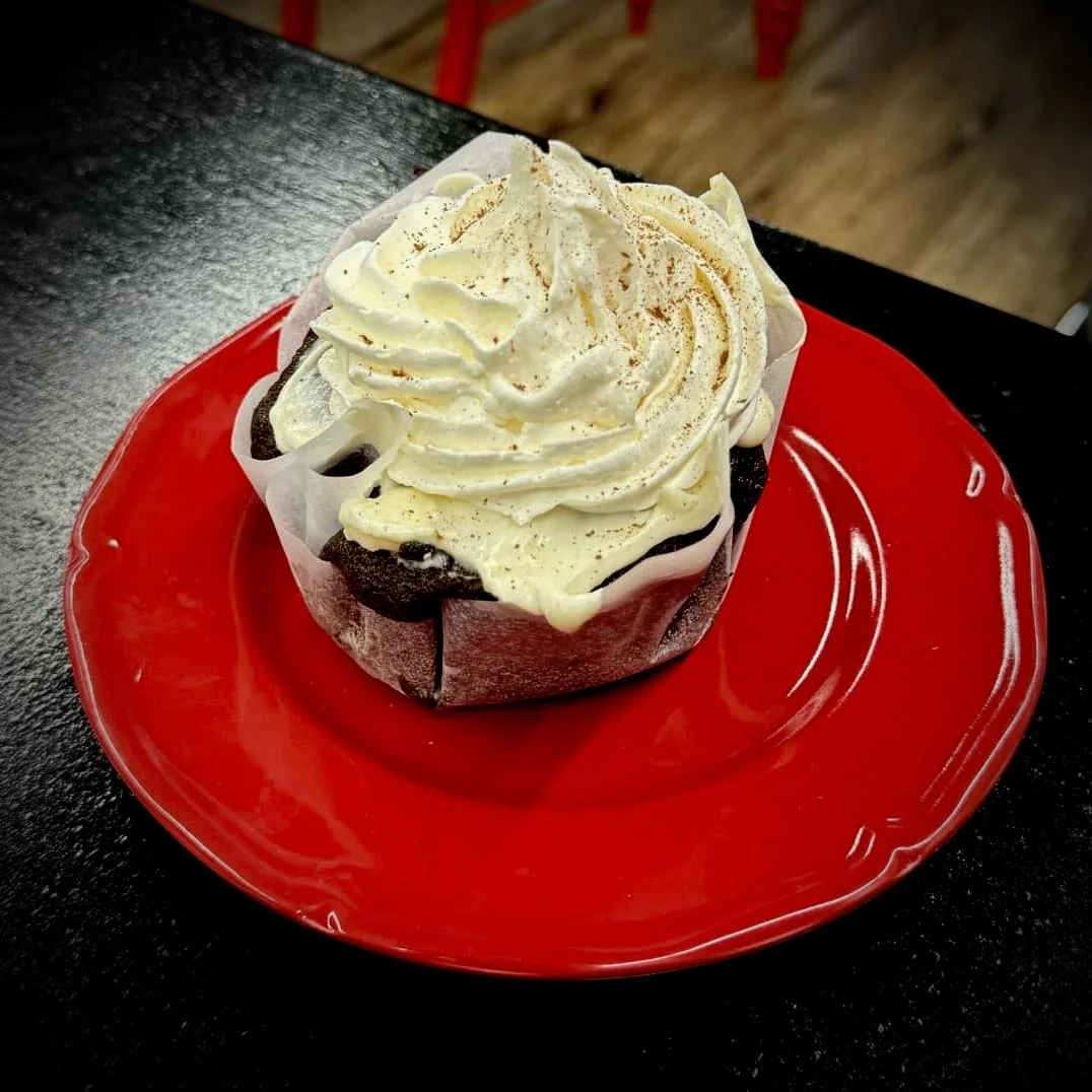 Chocolate muffin with whipped cream topping on a red plate.