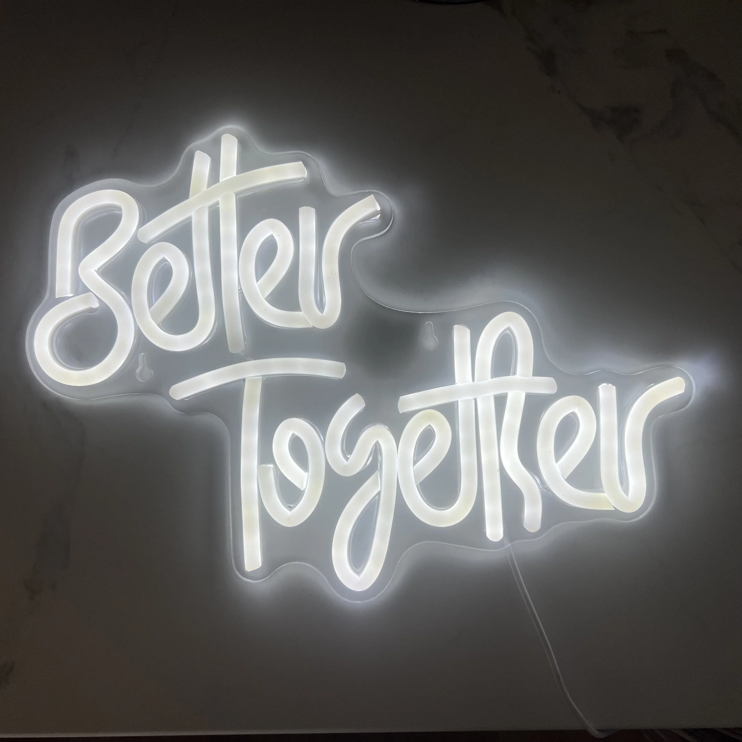 Neon sign with partially visible words in white lights on a gray wall.