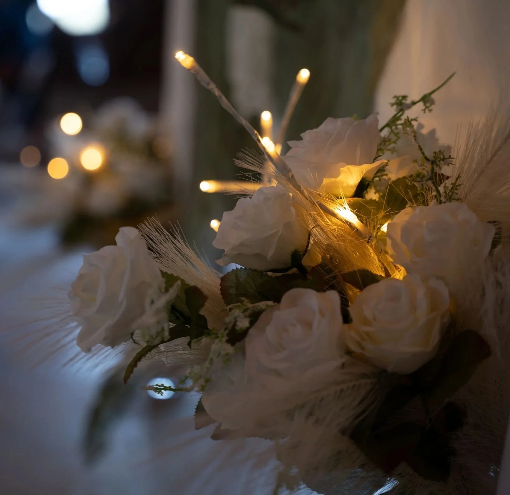 A floral arrangement with white flowers illuminated by small warm lights, with blurred background lights.