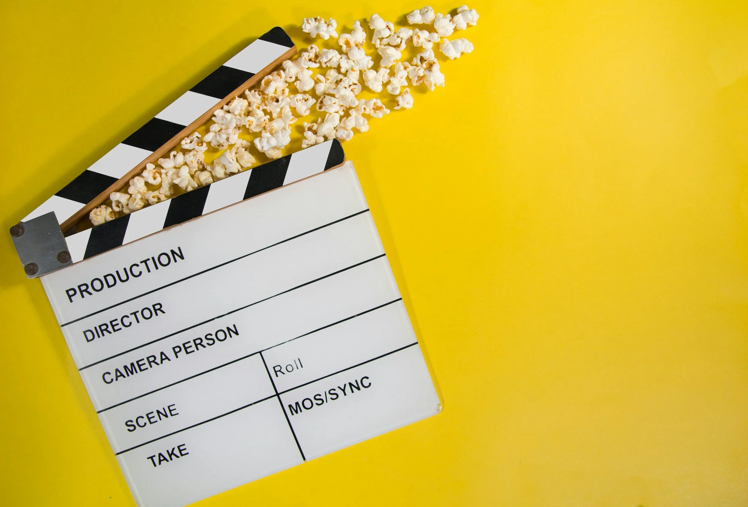 A director's clapperboard with popcorn spilling onto a bright yellow background.