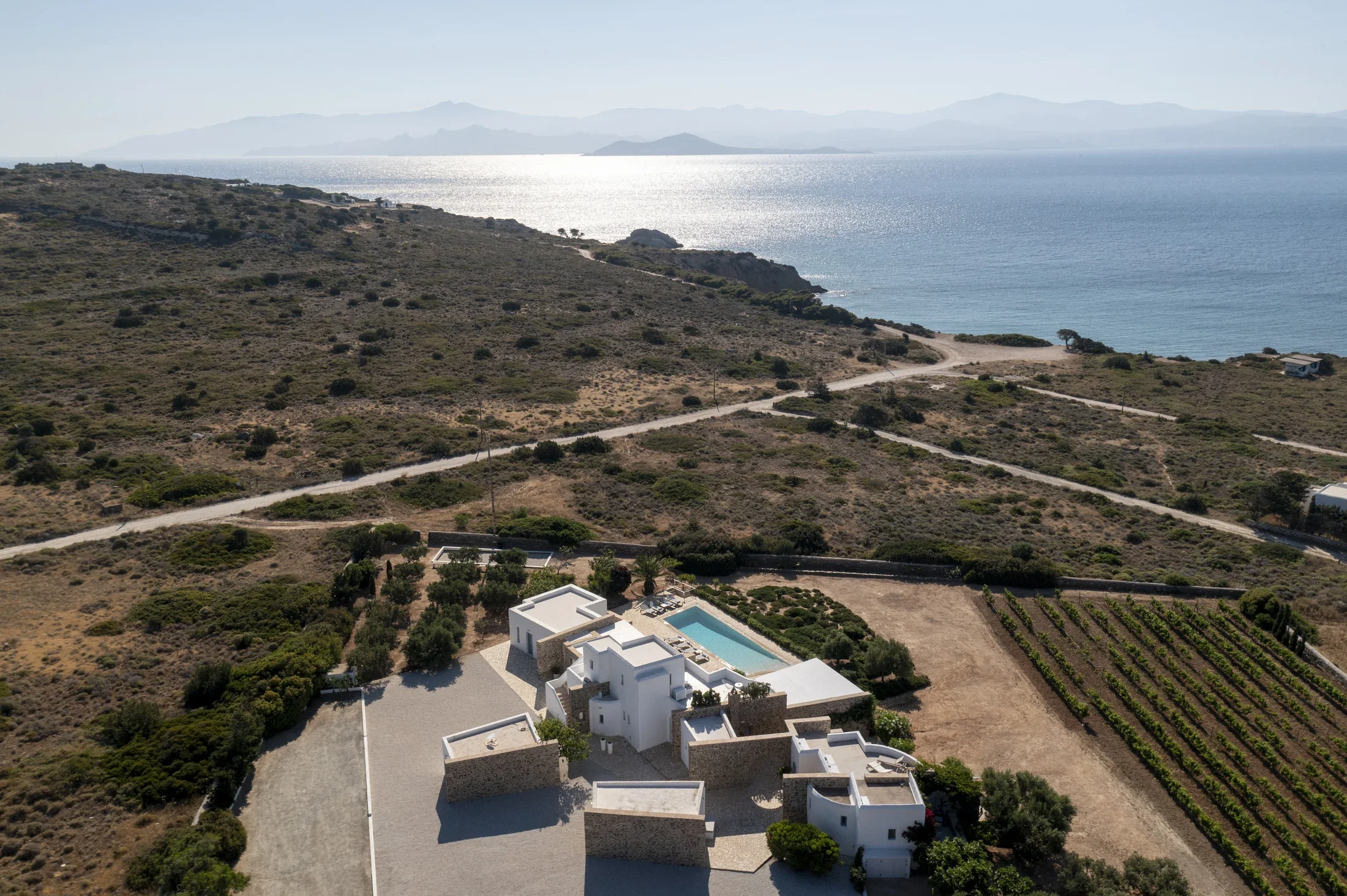 Aerial view of Villa Kavouraki, luxury villa in Paros, Cyclades, with private pool and sea view. The landscape includes hilly terrain leading to a Skalakia beach.