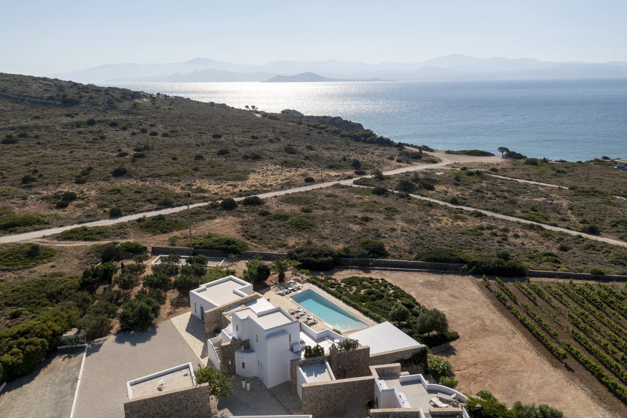 Aerial view of a modern white house with a swimming pool in a desert landscape, overlooking the ocean and distant mountains.