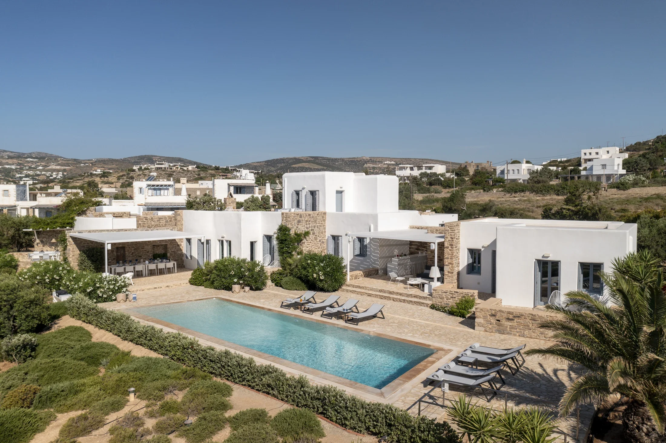 Side view of a luxurious villa with large outdoor swimming pool with lounge chairs, surrounded by  vineyards.