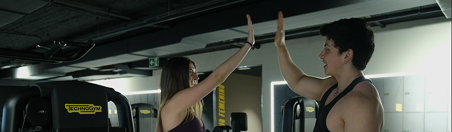 Dos personas en un gimnasio dándose un high five sobre la maquinaria de ejercicio.