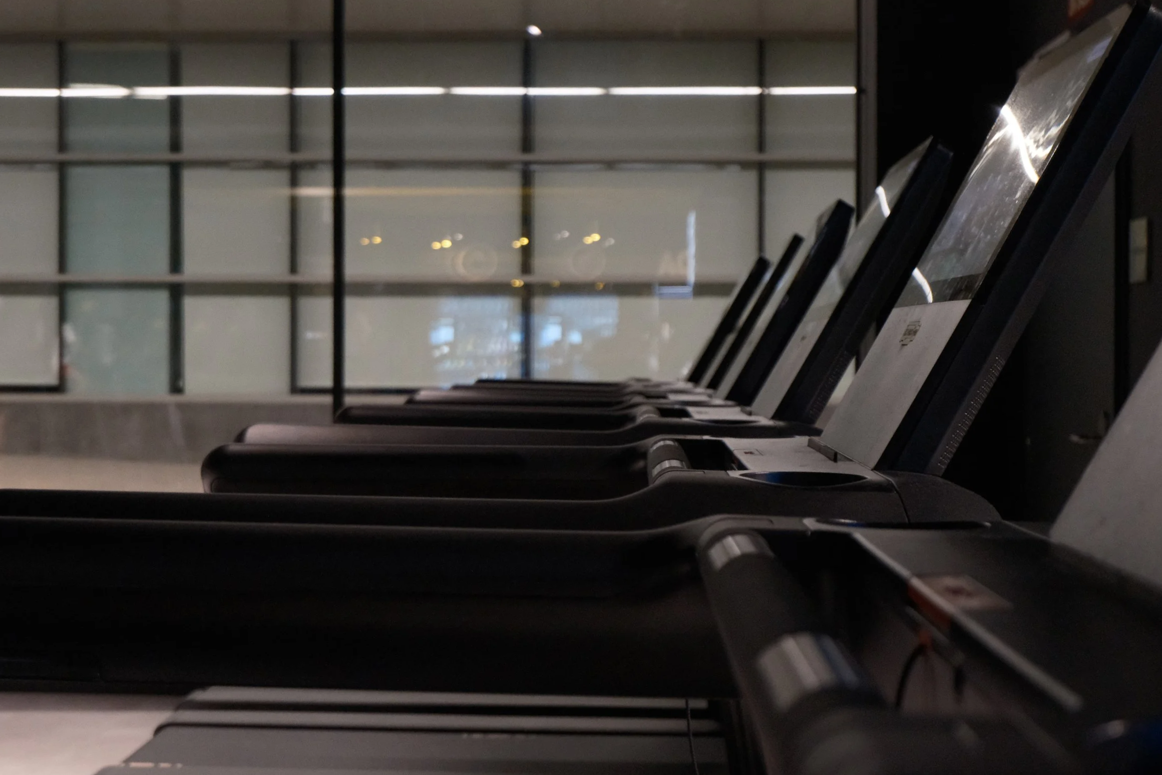 Filas de máquinas de pago en un aeropuerto o tienda, vista desde un ángulo lateral, con ventanas grandes al fondo