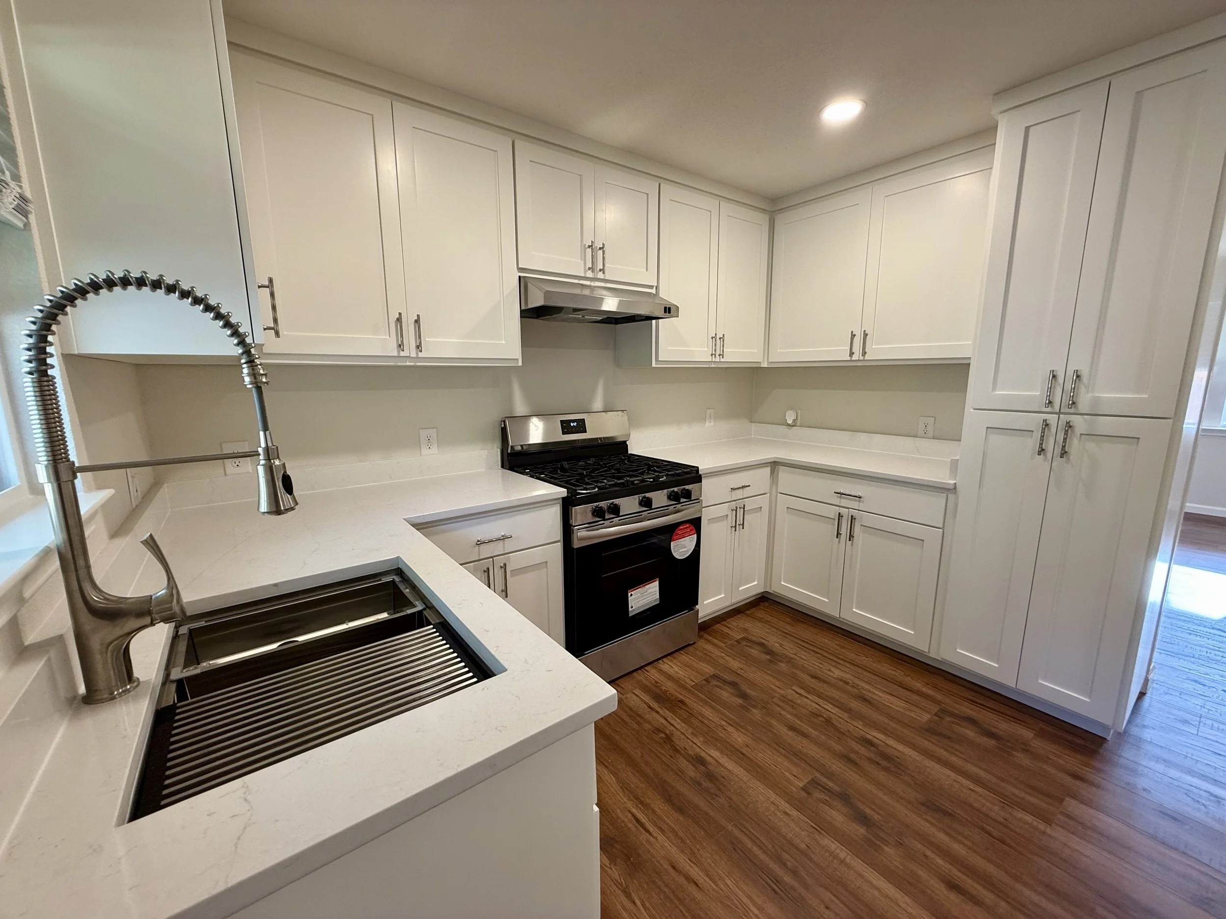 Modern kitchen with white cabinets, stainless steel stove, and dark wood flooring.