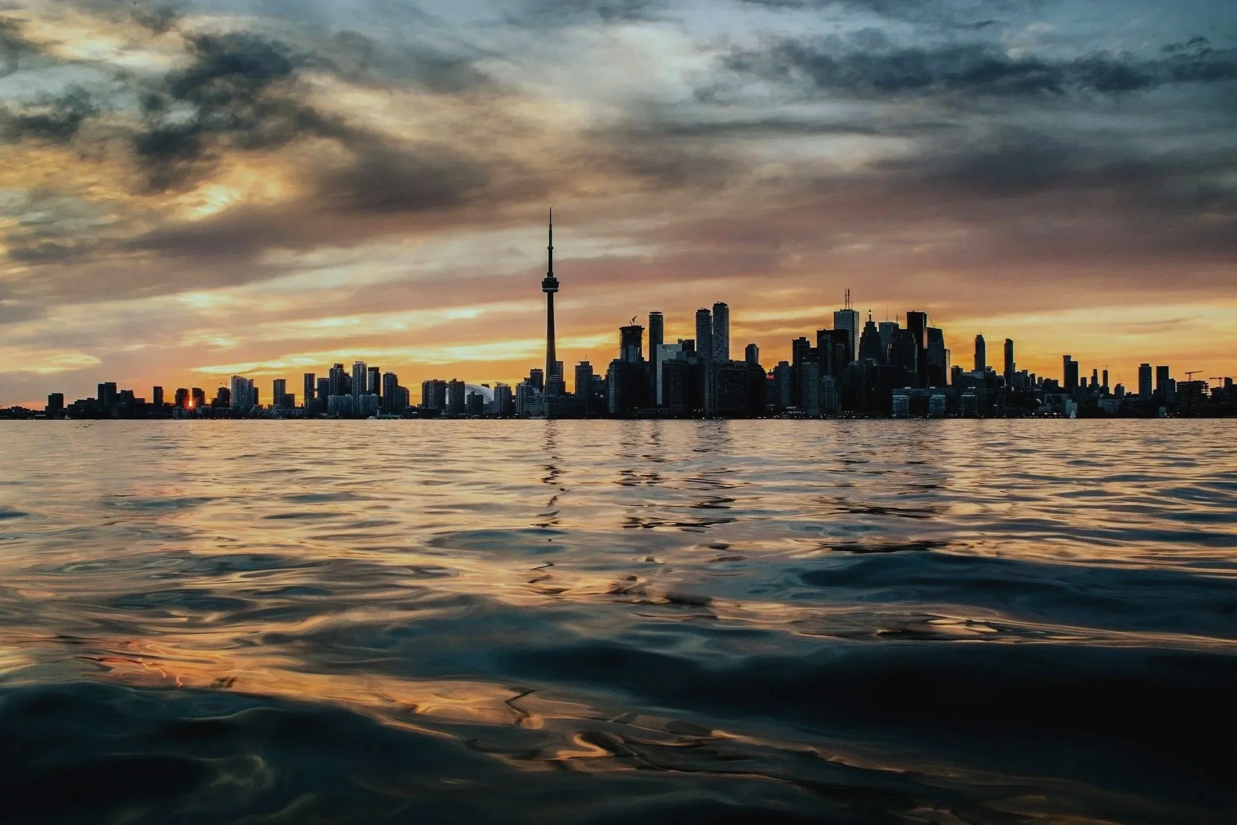 Toronto skyline with the CN Tower at sunset, viewed across rippling Lake Ontario