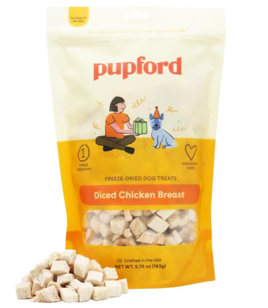 Pupford freeze-dried dog treats in a yellow and white bag labeled 'Diced Chicken Breast.' The illustration on the bag shows a girl sitting and petting a dog wearing a party hat, with a small pile of treats spilled in front.