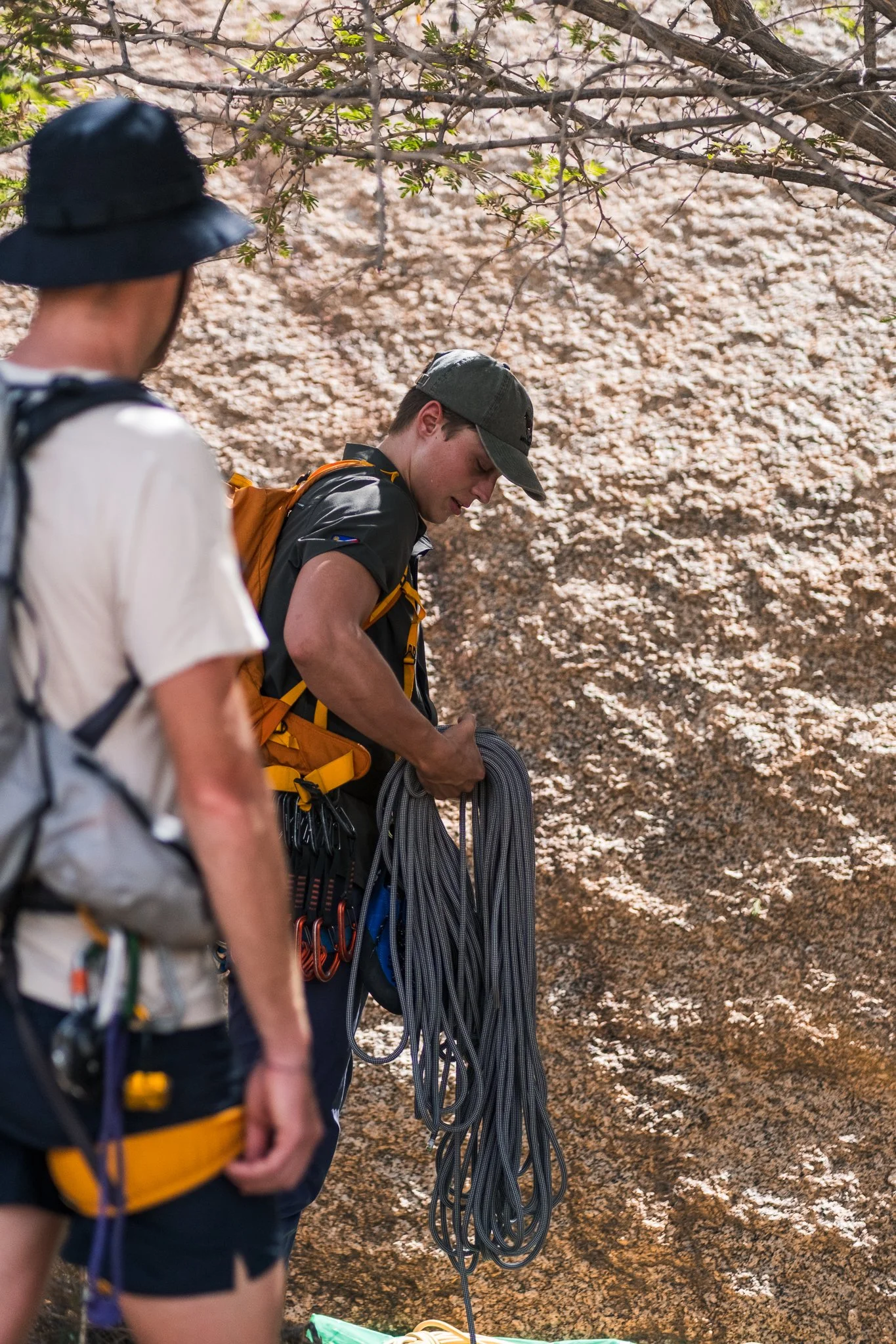 Two people preparing climbing gear outdoors with trees and rocks in the background.