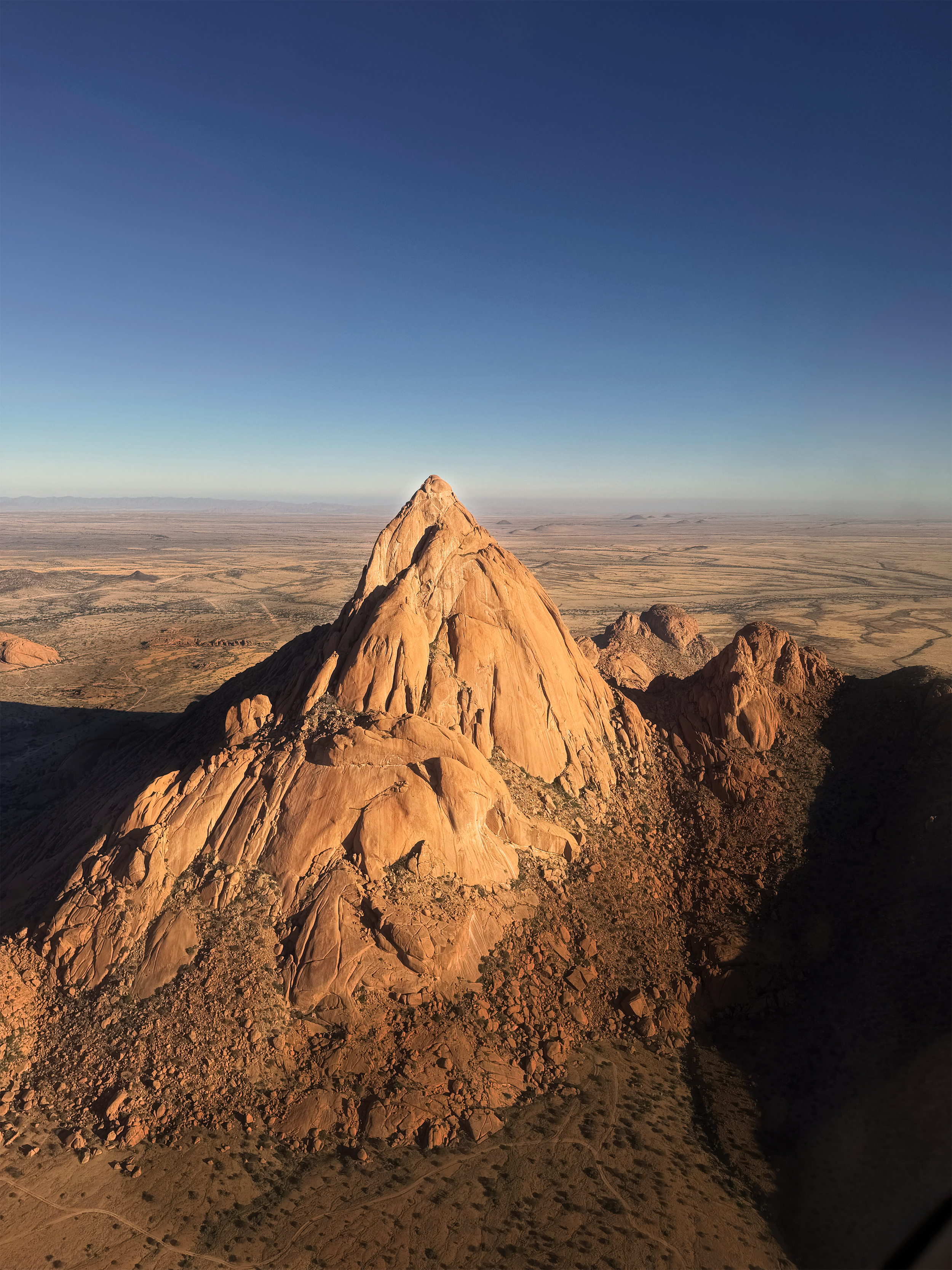 A rocky mountain peak in a desert landscape under a clear blue sky.