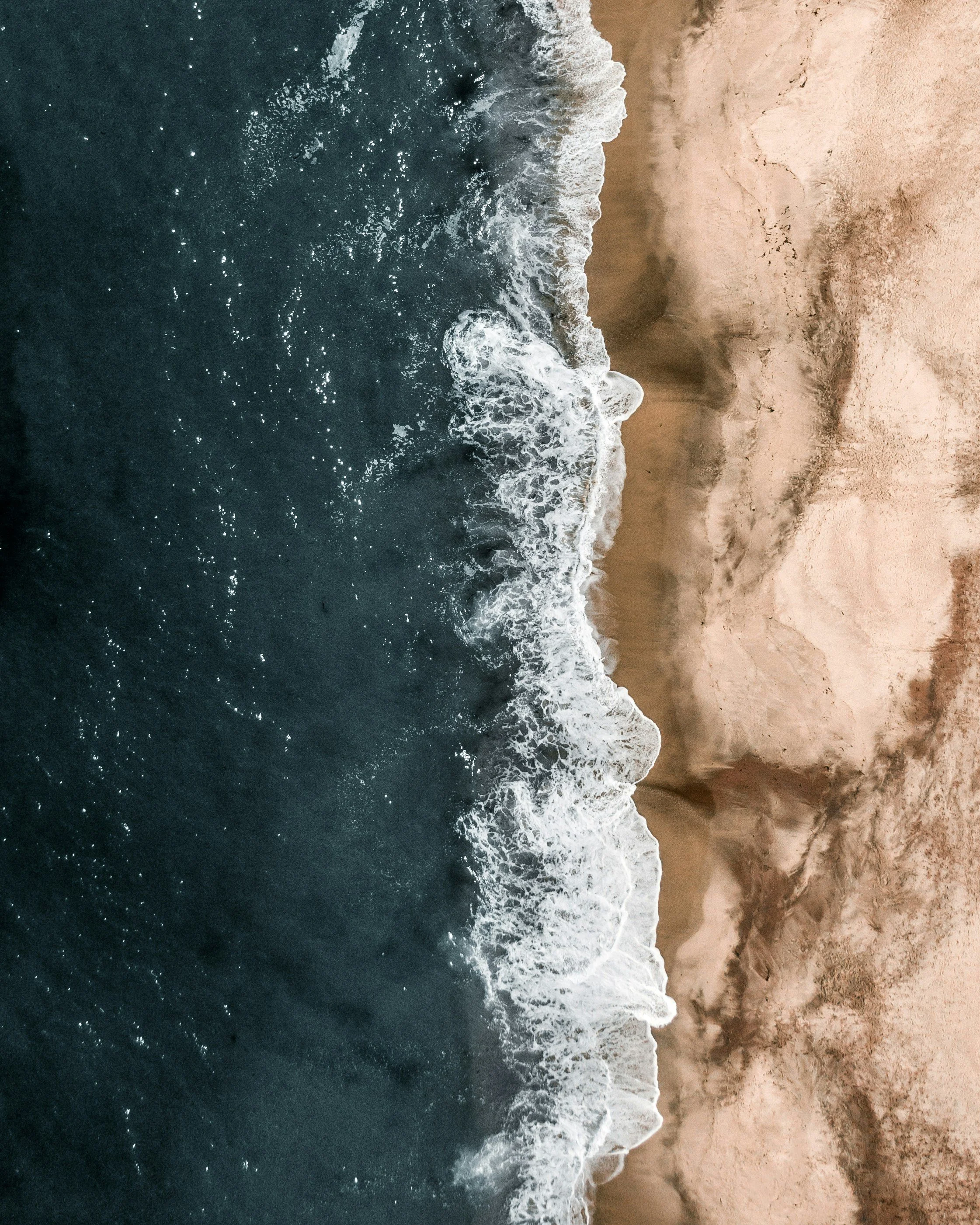 Aerial view of ocean waves crashing onto sandy beach shoreline.