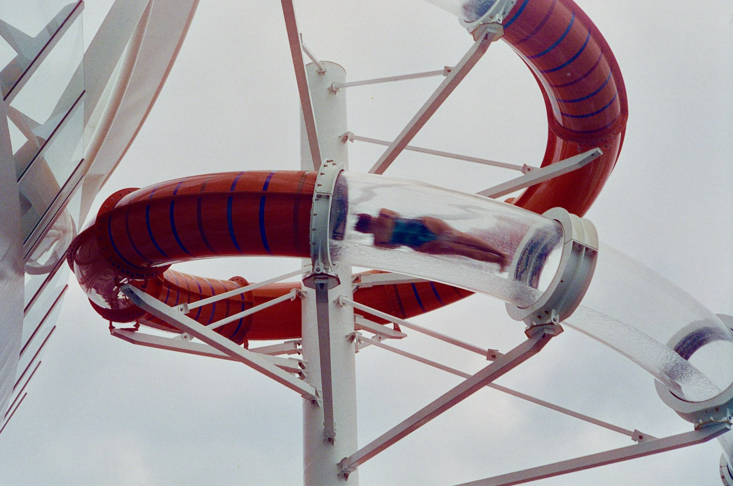 Close-up of a pink and red water slide on a Ferris wheel, with the cloudy sky in the background.