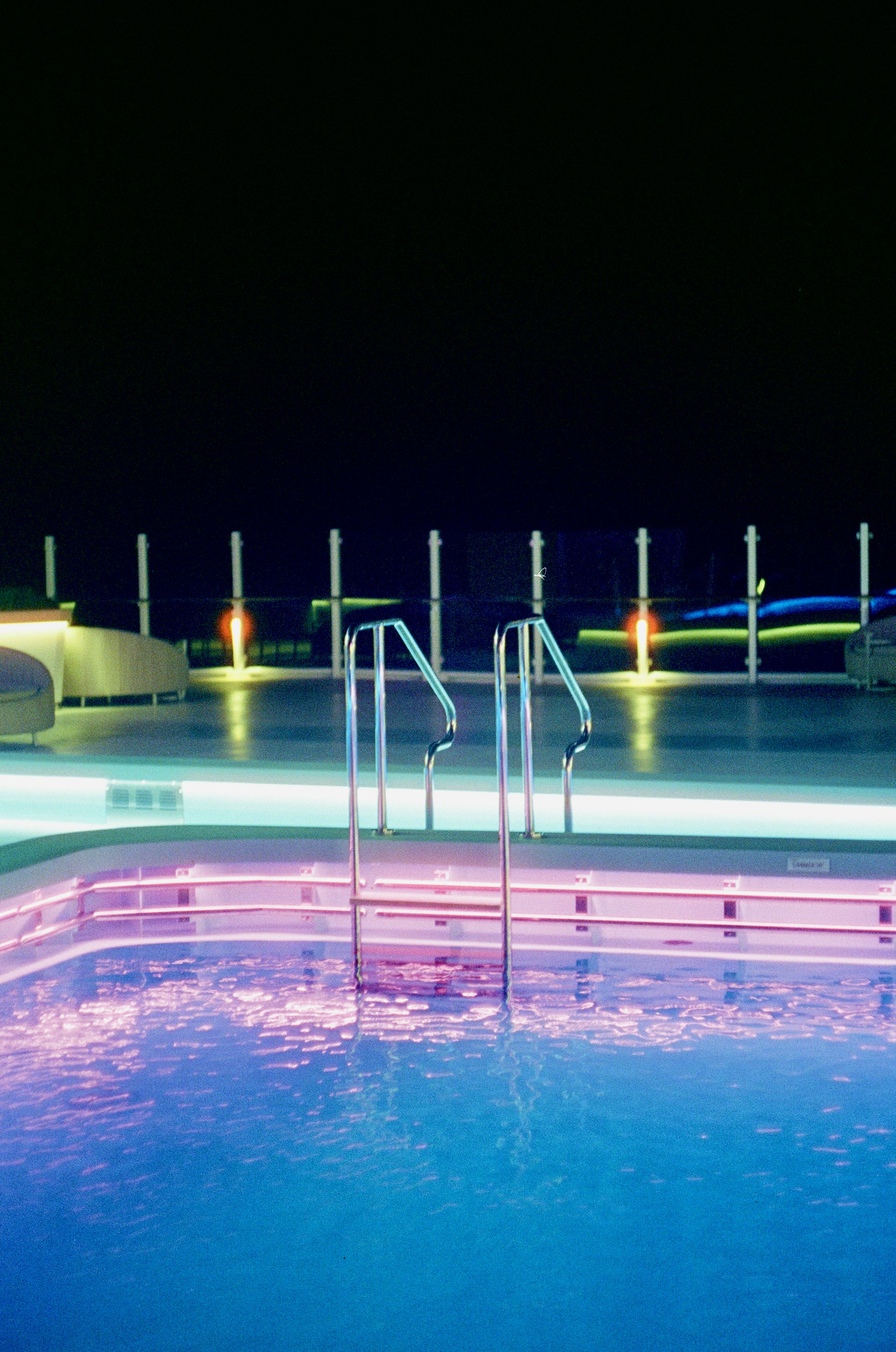 Empty swimming pool illuminated with colorful neon lights at night.