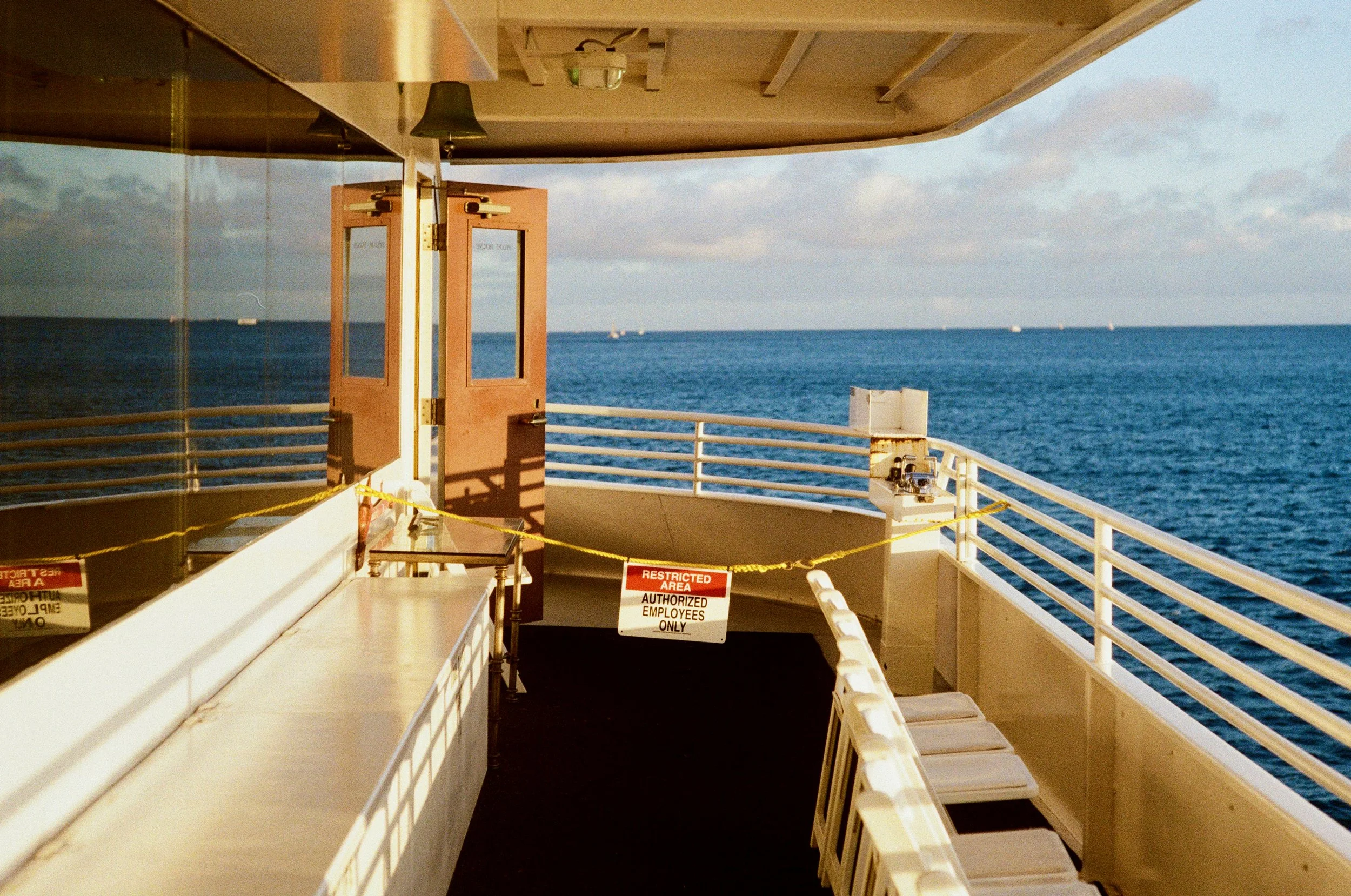View from a ship's deck showing the ocean and cloudy sky in the background, with safety signs and restricted area barriers.