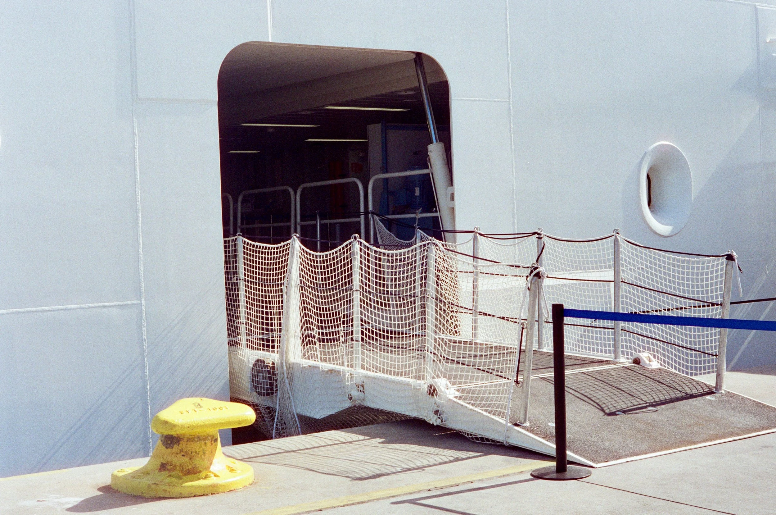 A section of the exterior of a cruise ship with a boarding ramp and safety netting.