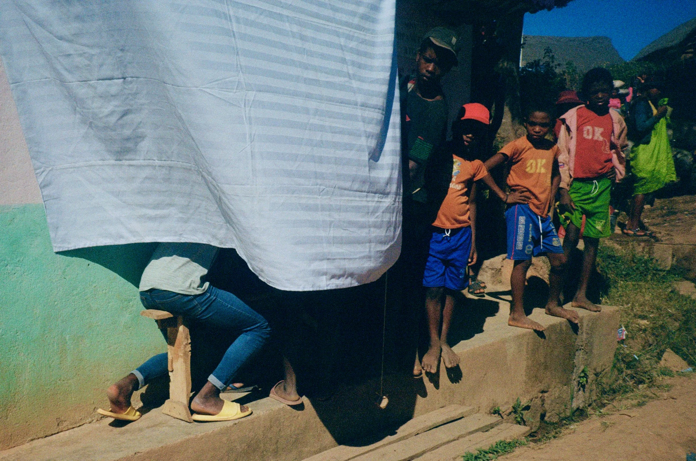 People standing in line outdoors in front of a painted wall and a mountain landscape background.
