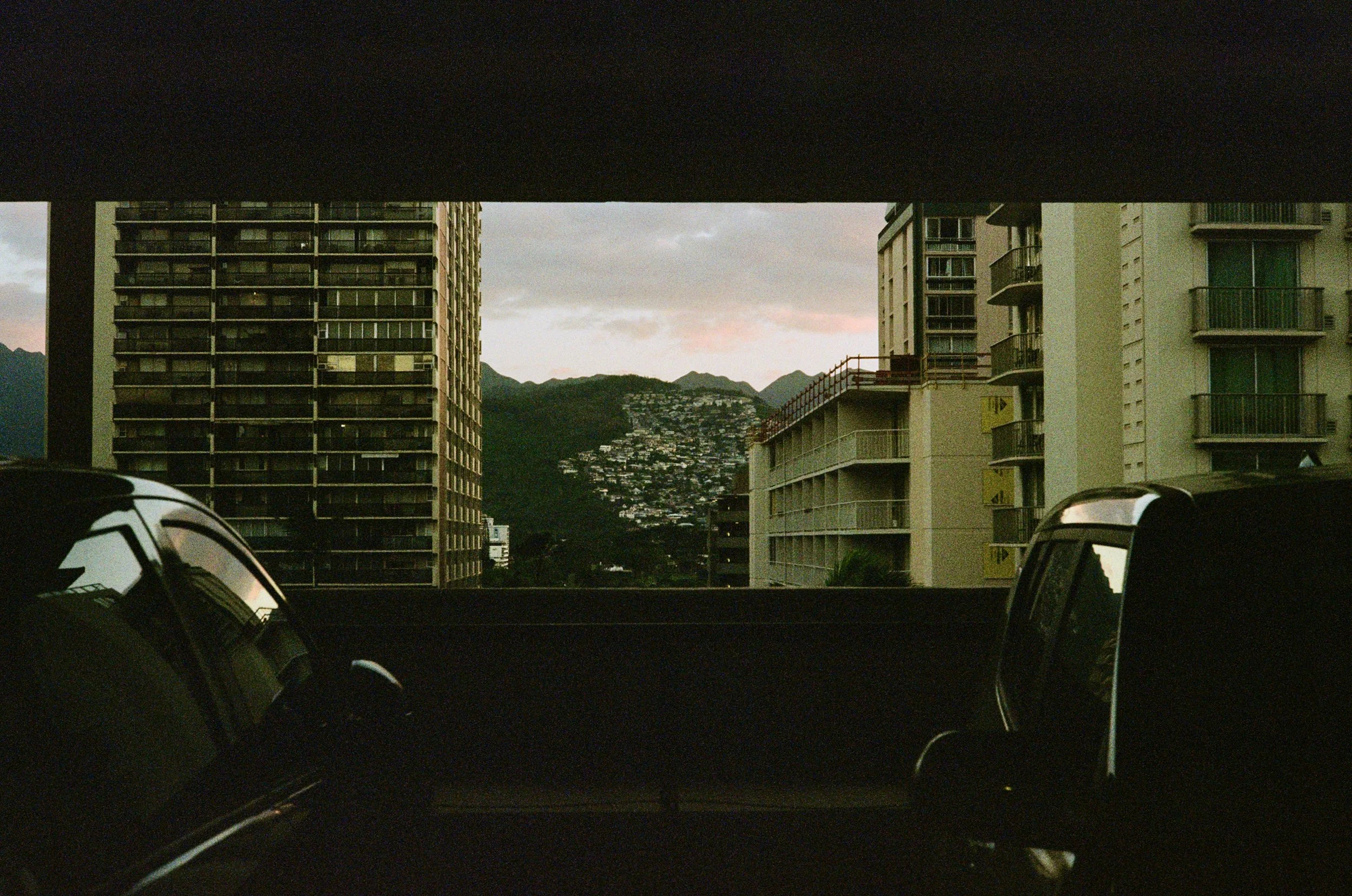 View from a parking garage showing two high-rise apartment buildings and mountains in the background during dusk.