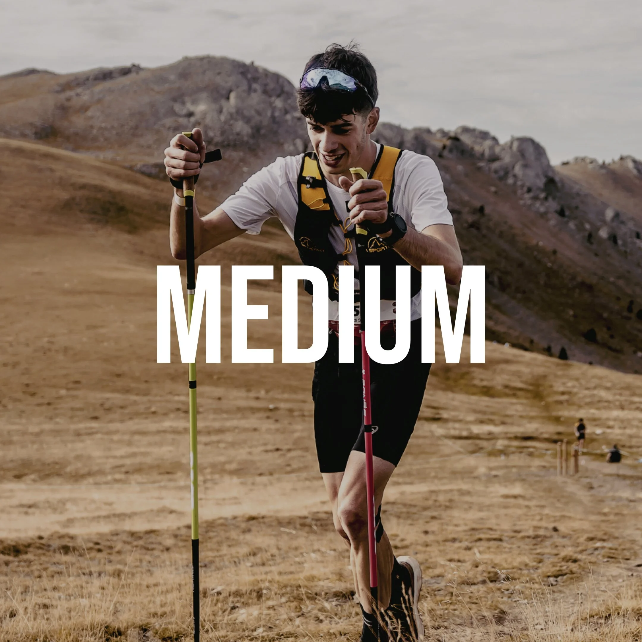 Joven en un paisaje árido participa en una carrera de larga distancia, usando bastones y ropa deportiva, con montañas al fondo.