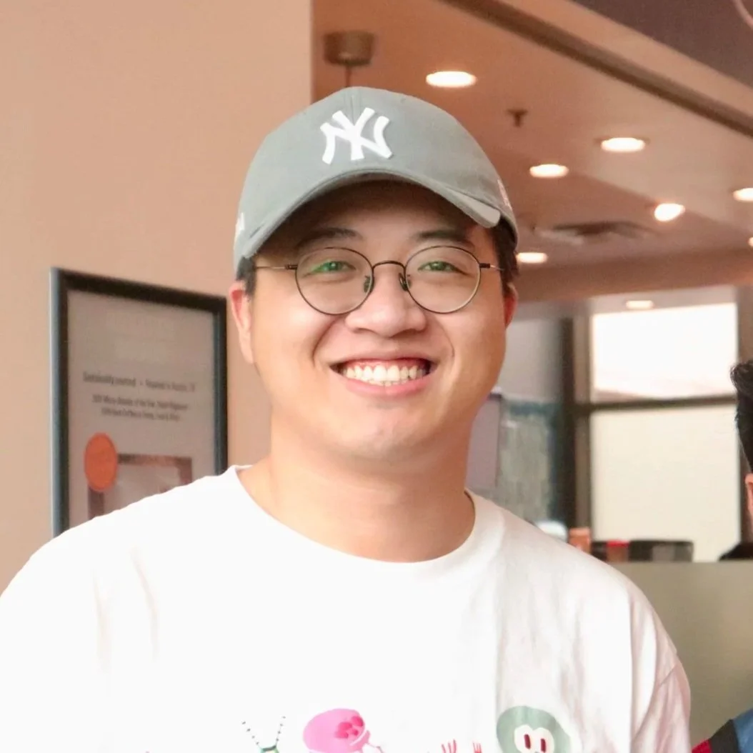 Young man wearing glasses and a gray New York Yankees baseball cap, smiling in an indoor setting.