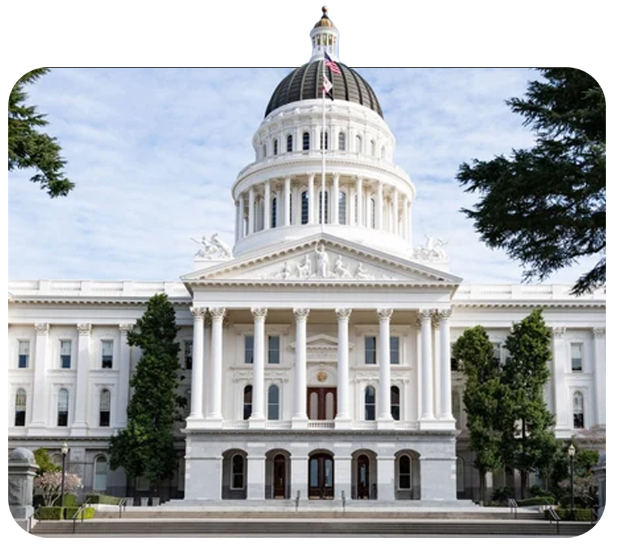 The California State Capitol building in Sacramento, California, with its white facade, large columns, and a dome topped with a flag, surrounded by trees and steps.