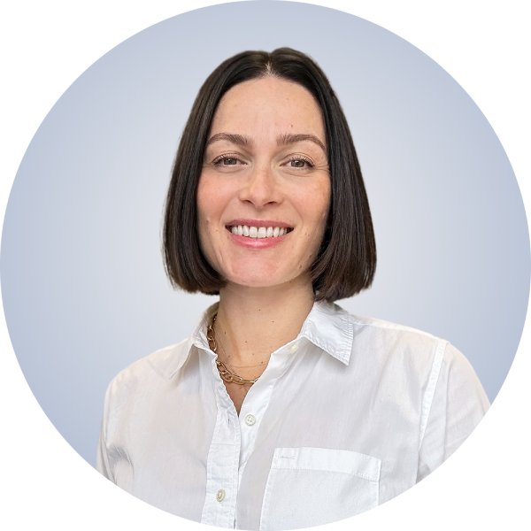 A woman with shoulder-length dark hair smiling, wearing a white button-up shirt and a gold necklace, standing against a light gray background with a black and blue graphic element in the upper left corner.