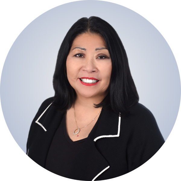 Professional woman with black hair, red lipstick, wearing a black blazer with white piping and a black top, smiling in front of a light gray background.